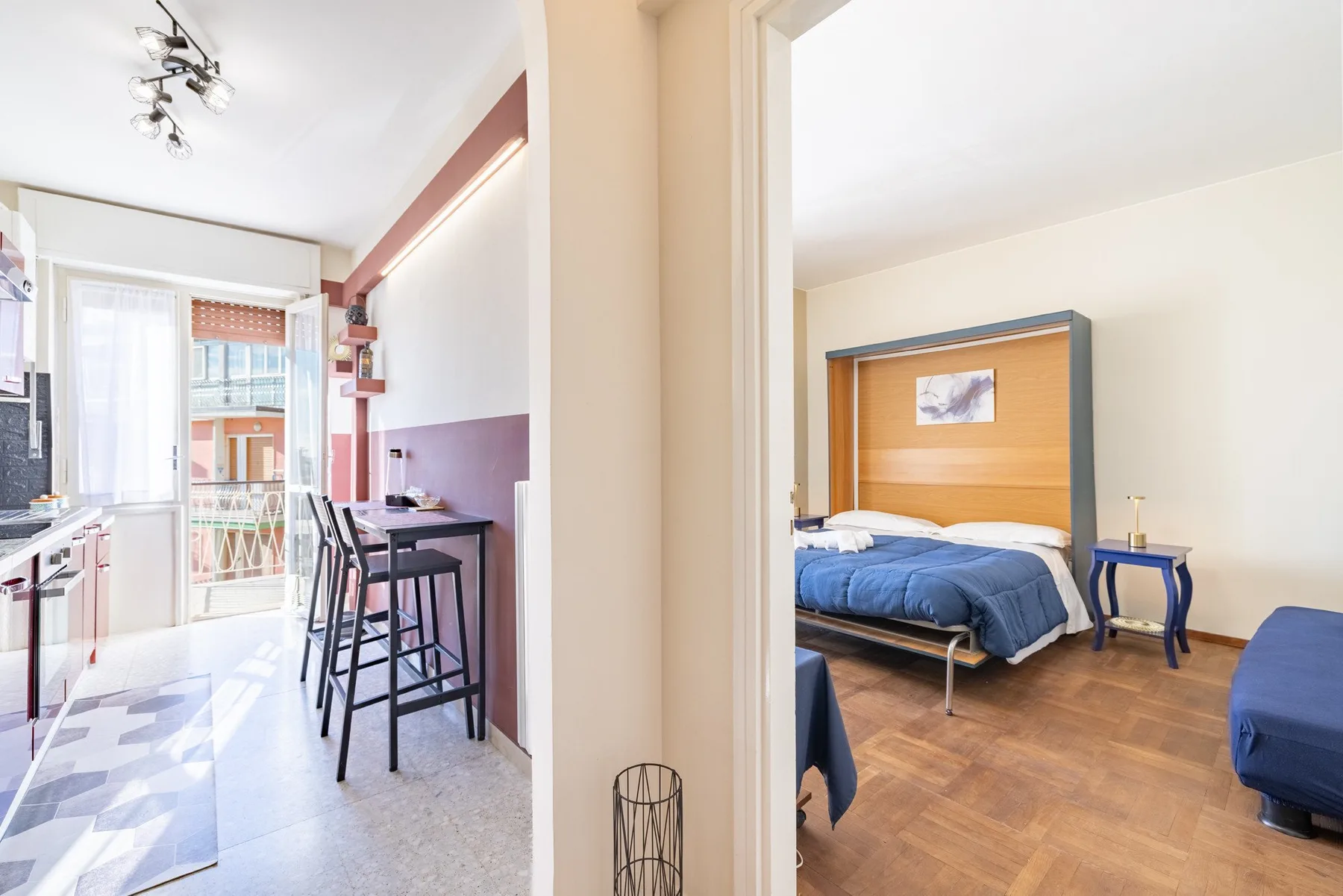 A compact kitchen and dining area opens beside a bedroom with blue bedding.