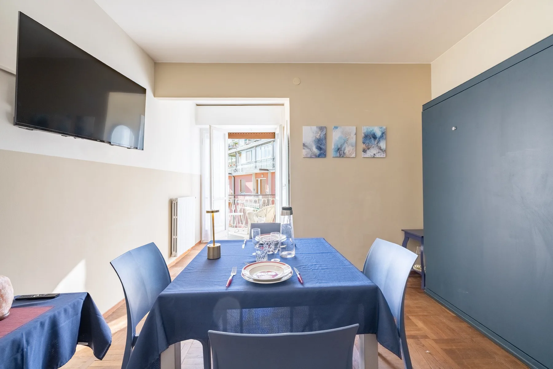 A dining area with a blue tablecloth-covered table and a wall-mounted television.