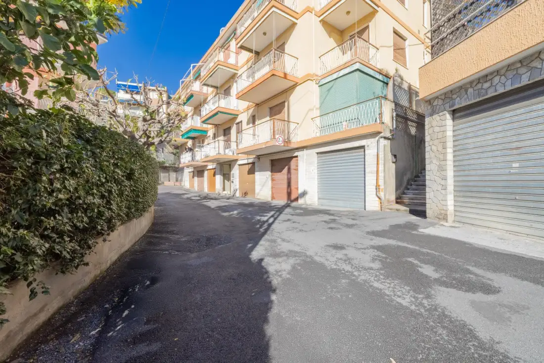 A paved lane runs beside apartment buildings with balconies and garage doors.
