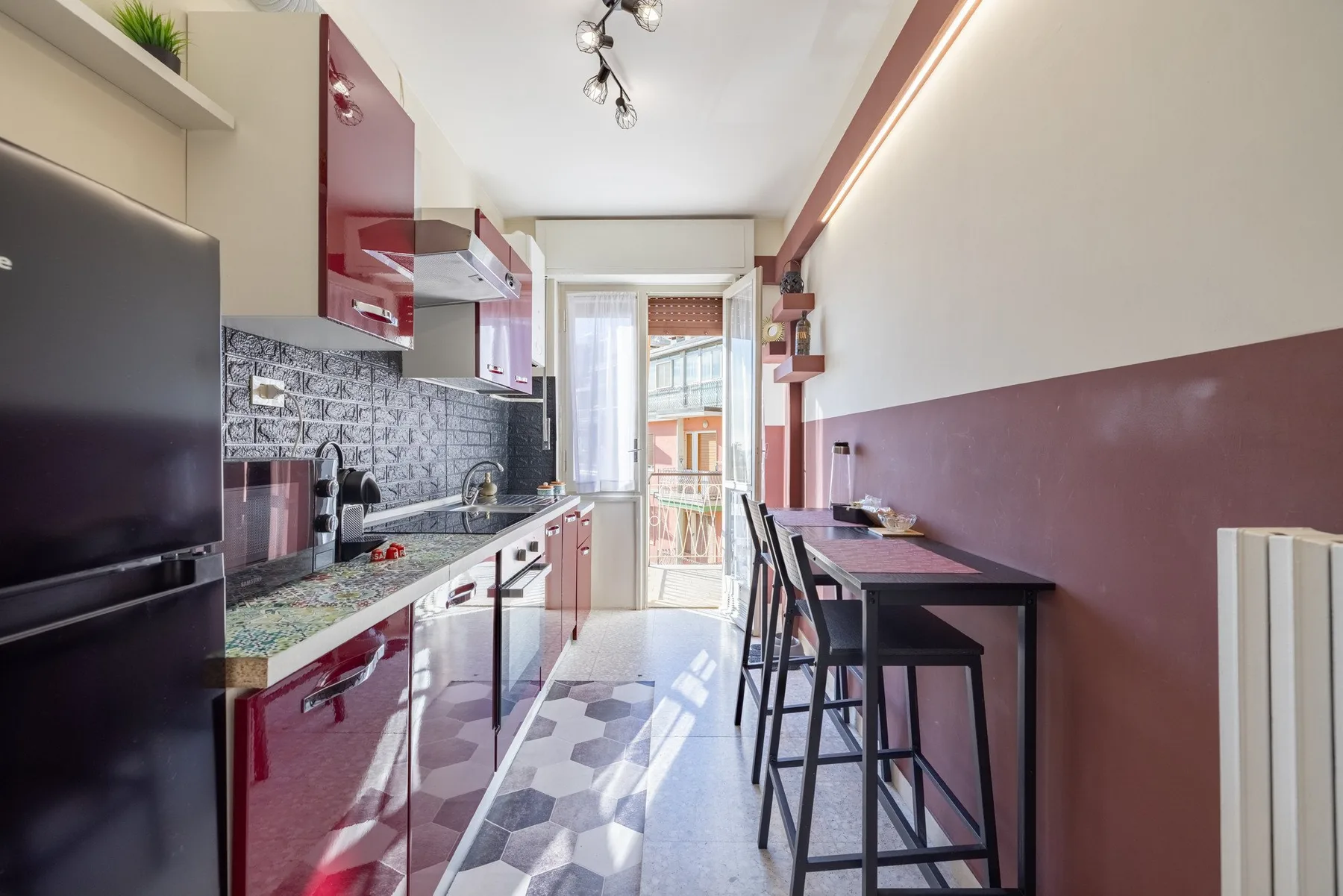 A narrow kitchen and dining area with glossy red cabinets and a counter-height table.