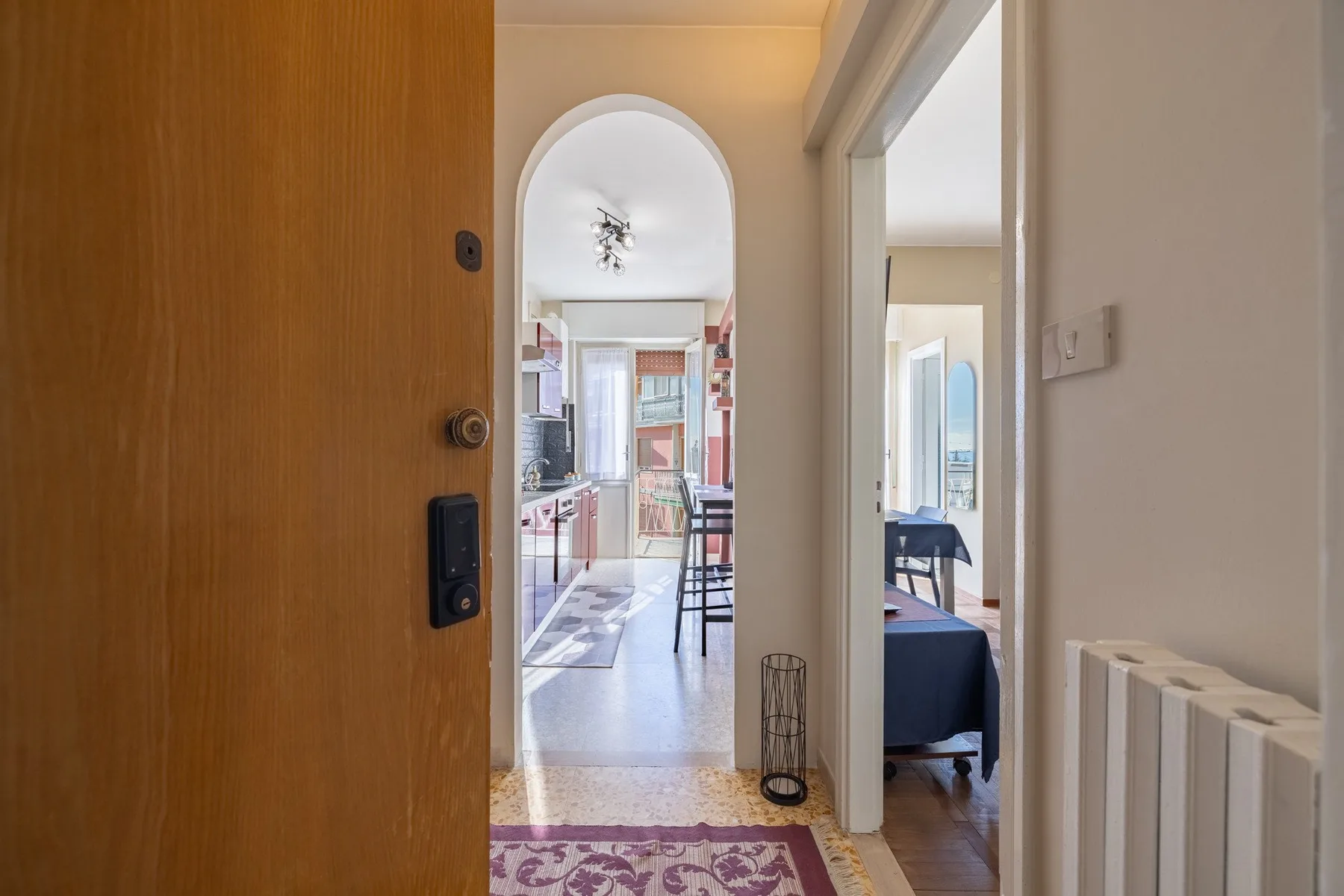 An open doorway looks toward a bright kitchen and a bedroom.
