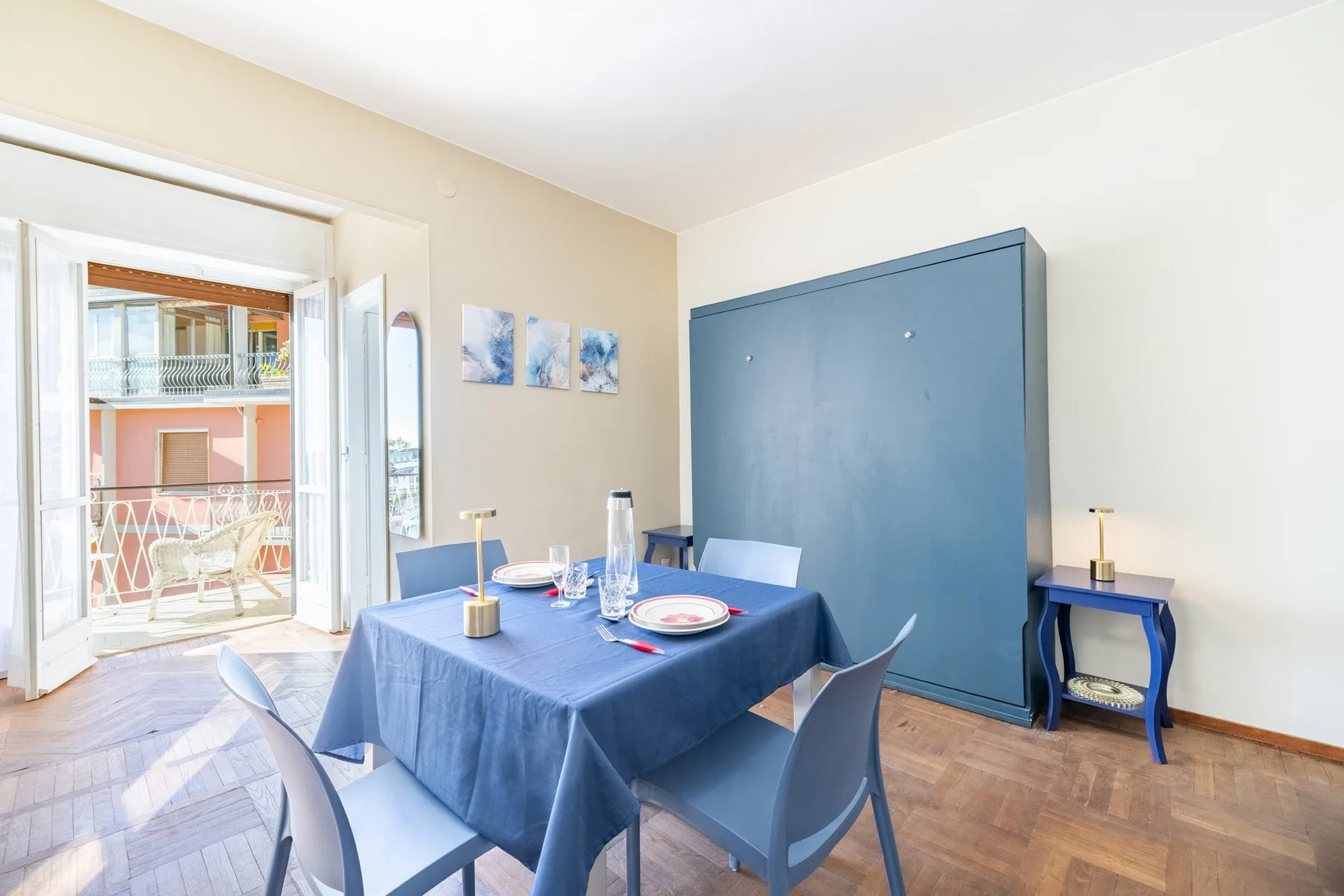 A dining area with a blue-covered table and chairs beside an open balcony door.