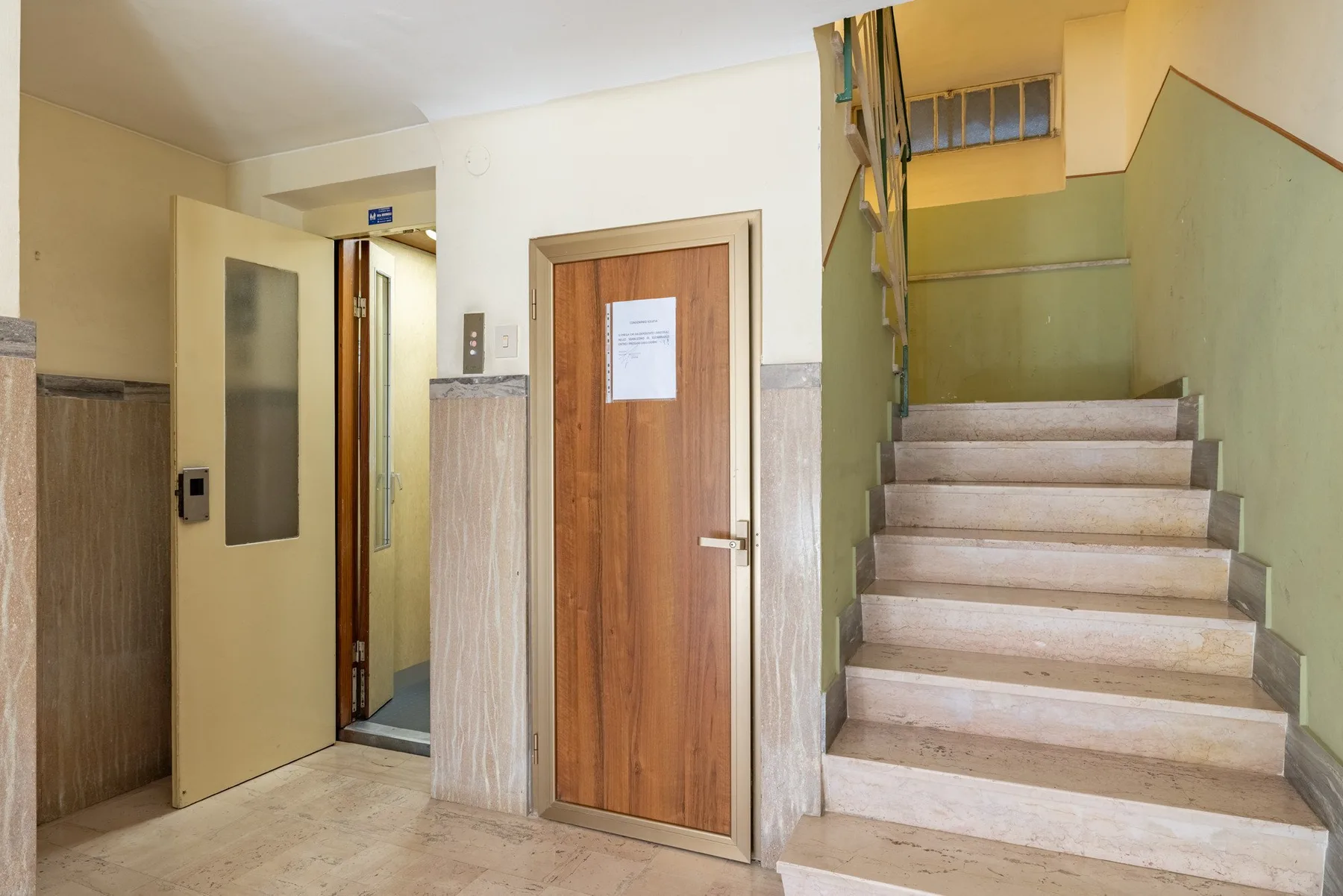 An indoor stairwell with a wooden door and an open doorway.