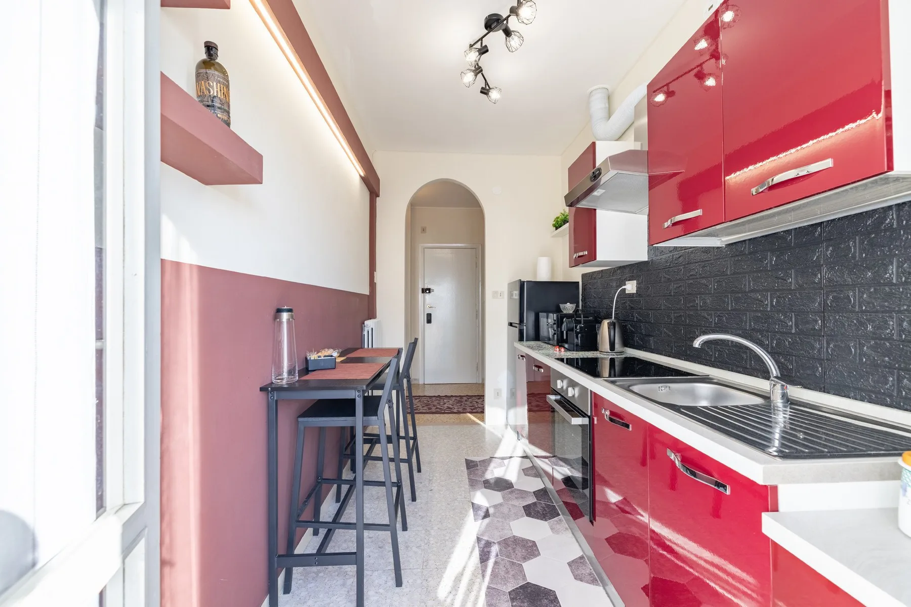 A narrow kitchen with red cabinets, a sink, and a small dining area.