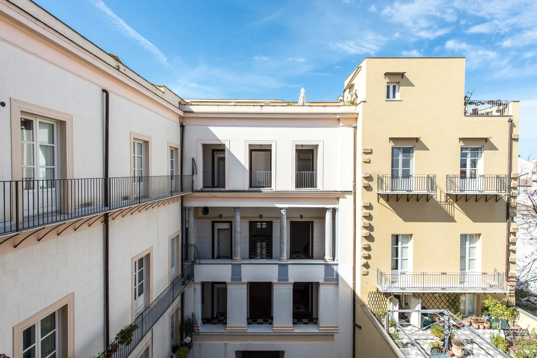 A sunlit courtyard framed by pale buildings with balconies and windows.