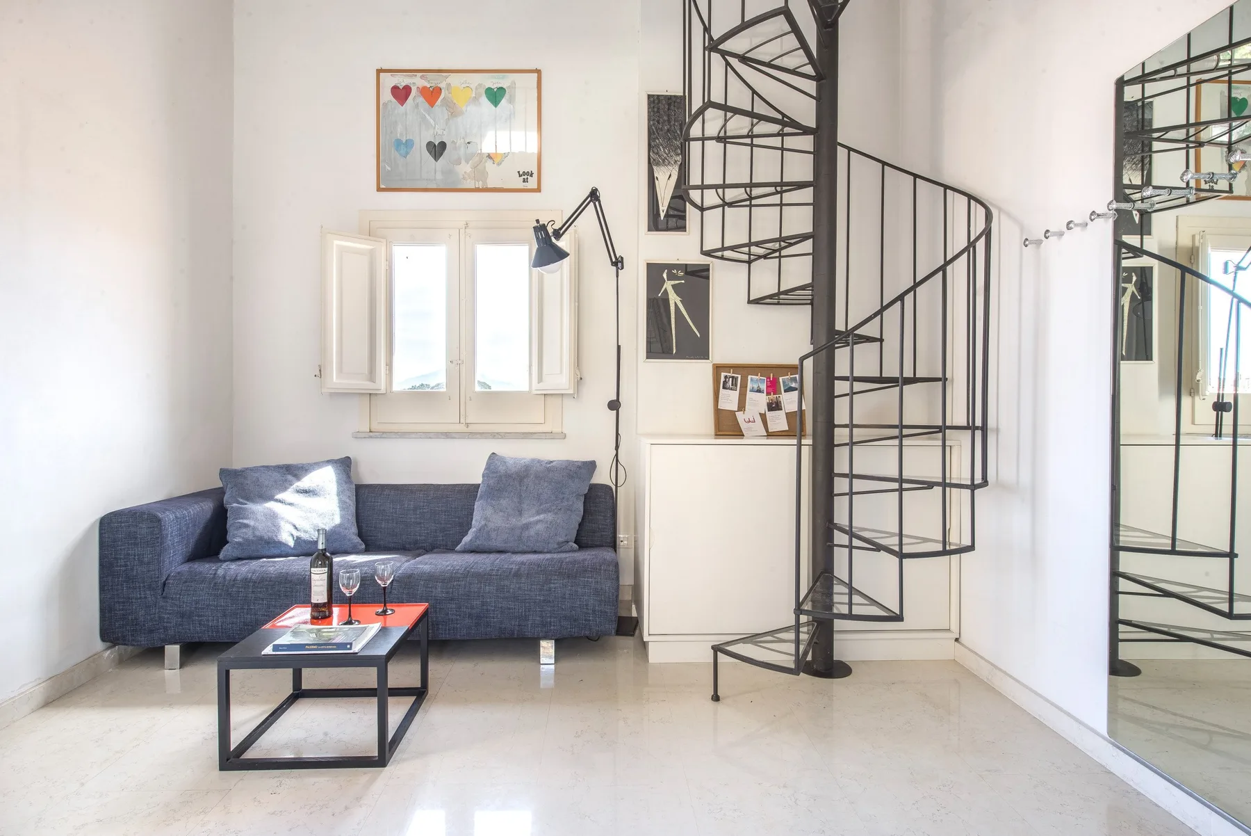A bright living room with a blue sofa and a spiral staircase.