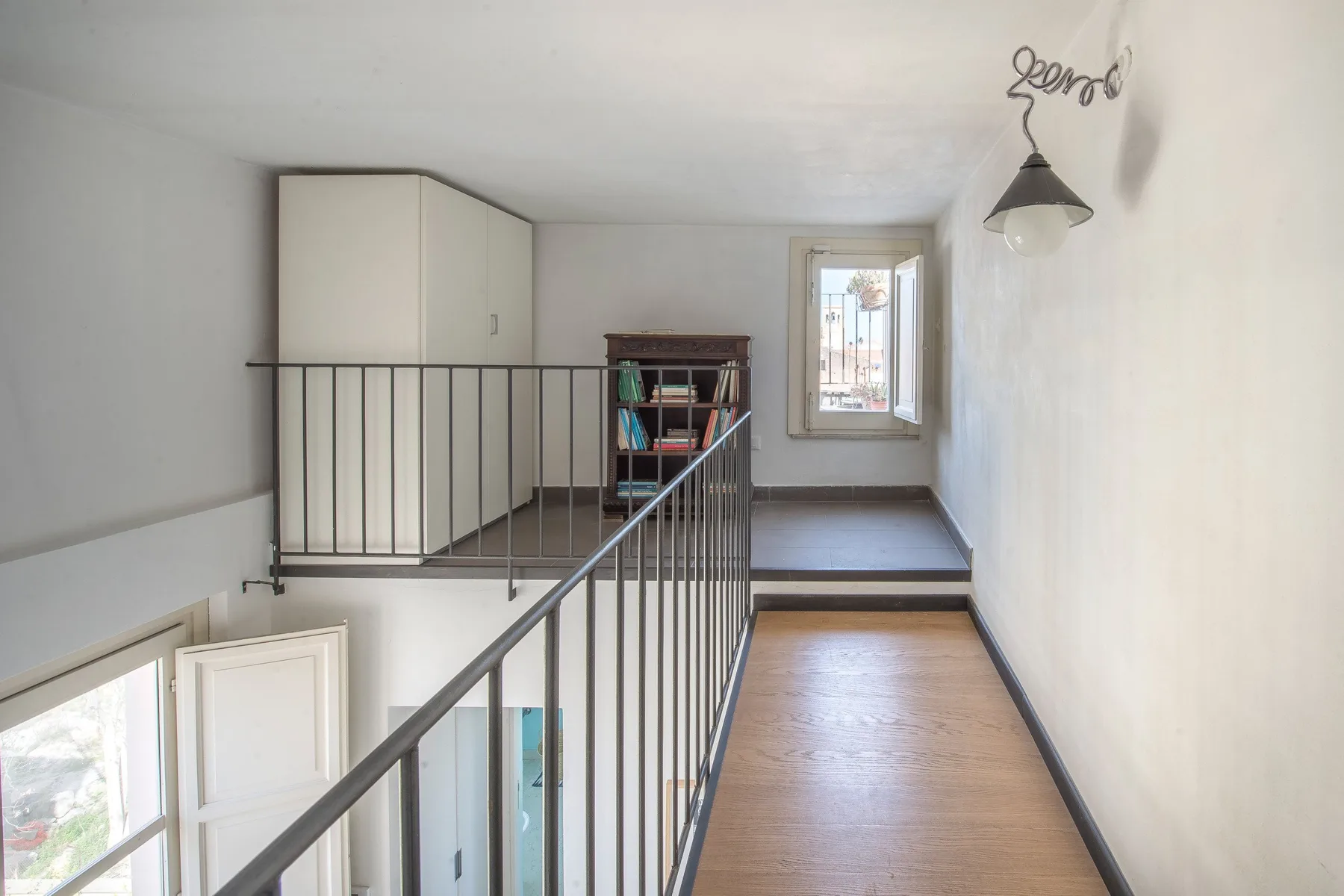 An interior landing with a metal railing, a cabinet, and a window.