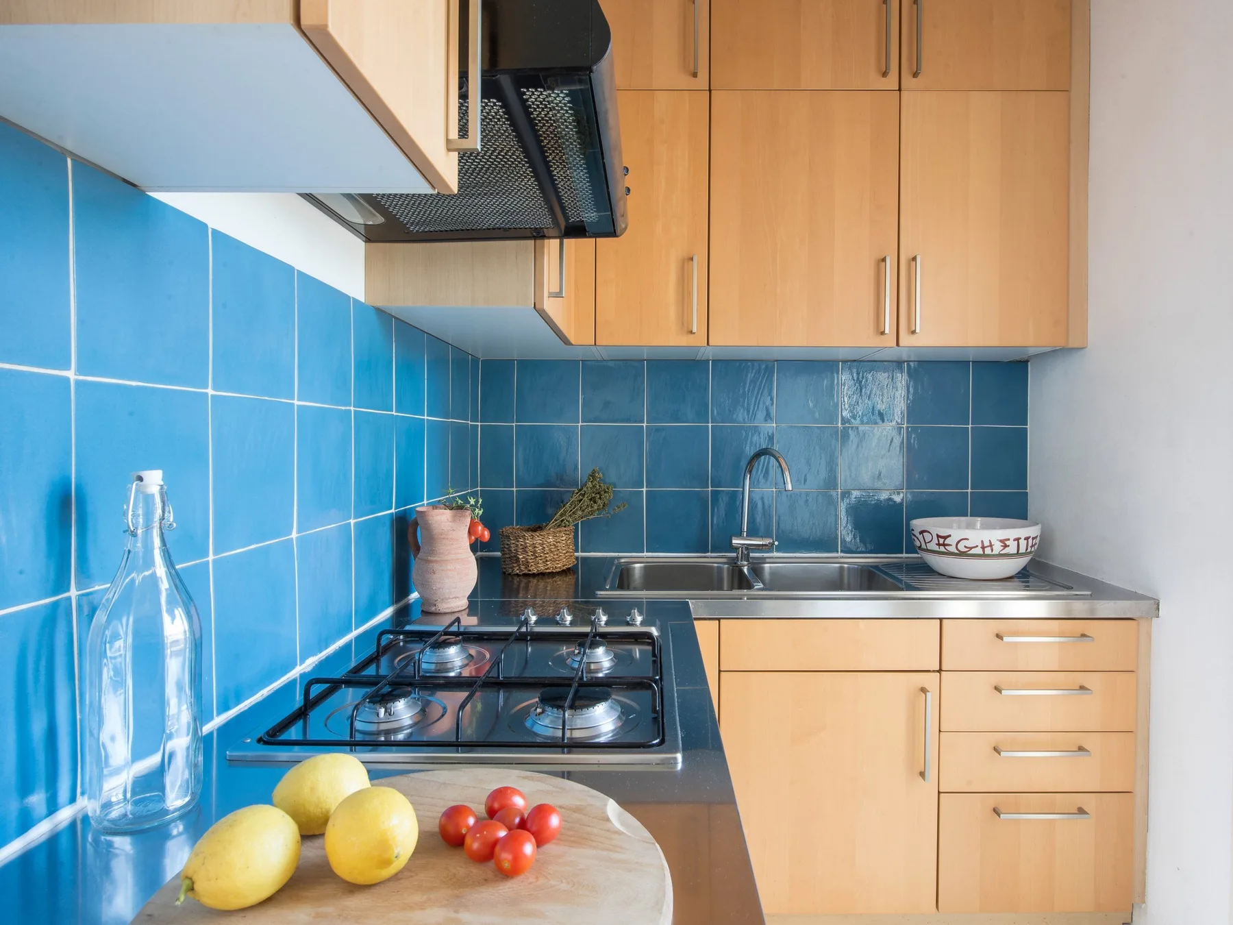 A compact kitchen with blue tiled walls, wooden cabinets, and a countertop stove.