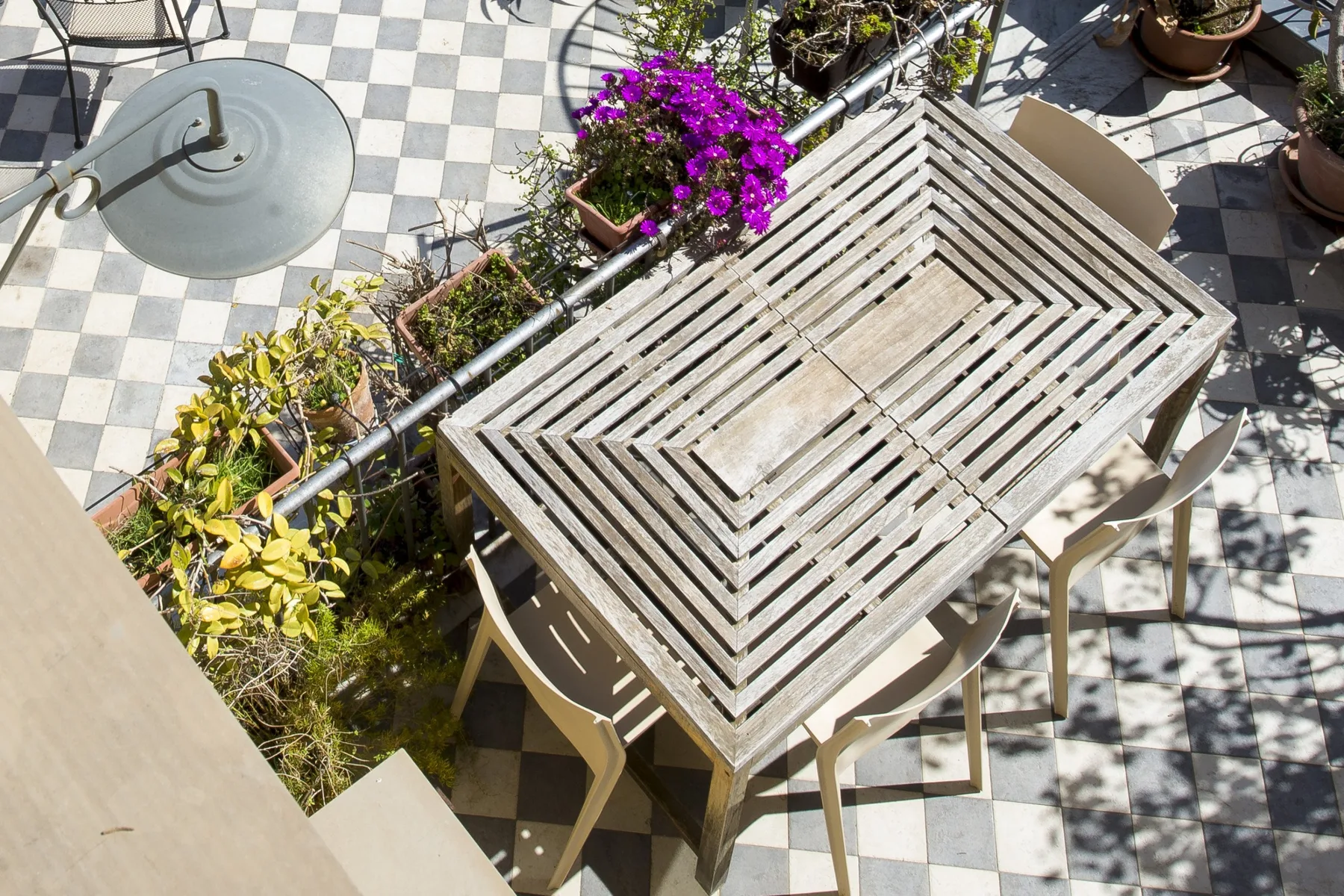 An outdoor patio dining area with a slatted table and potted flowers.