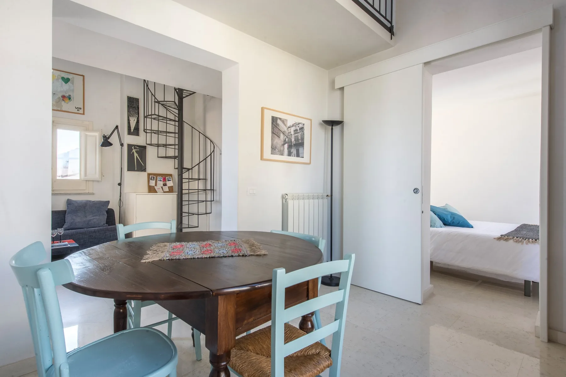 A dining area with a round table and chairs opens onto a bedroom.