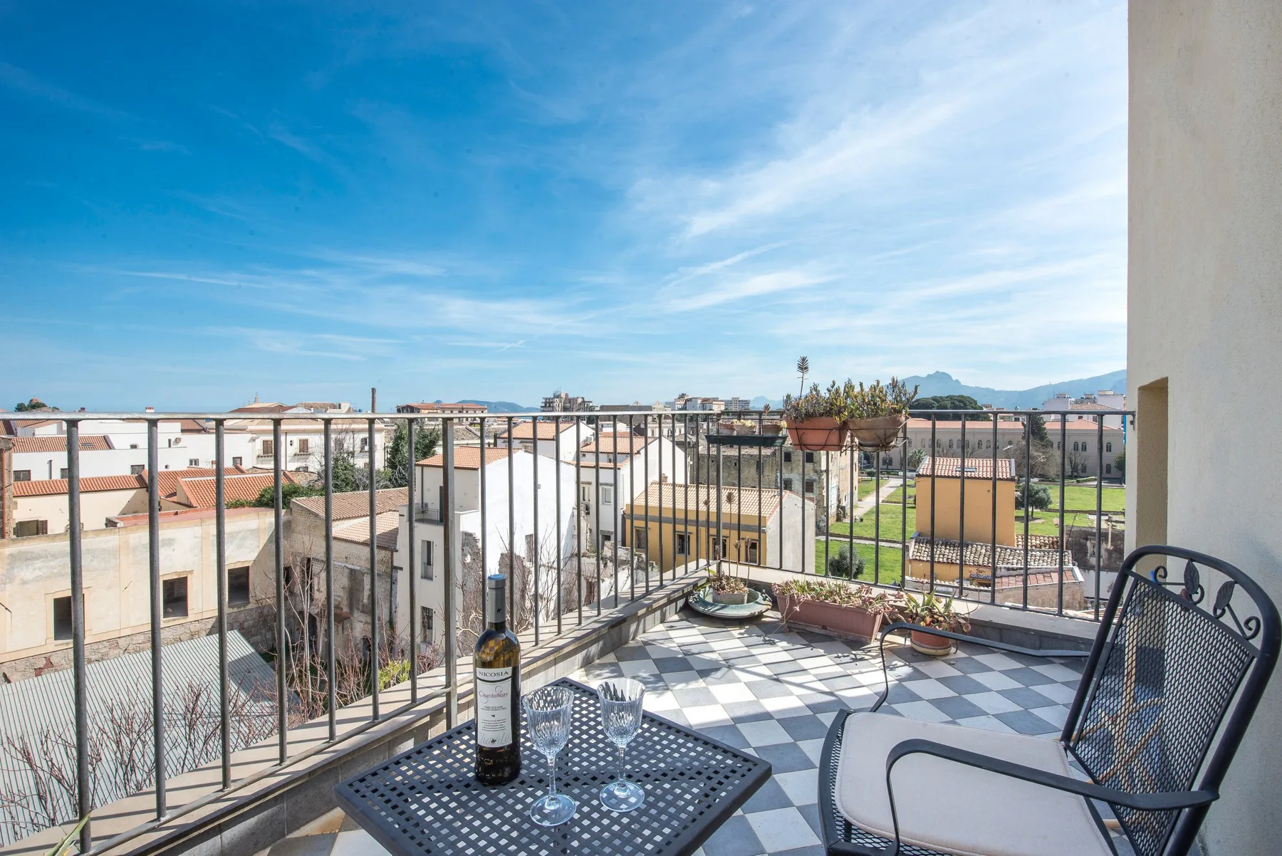 A balcony seating area overlooks nearby rooftops beneath a bright blue sky.
