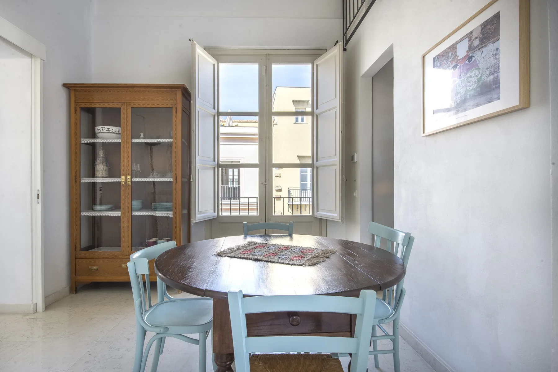 A bright dining area with a round wooden table and an open window.