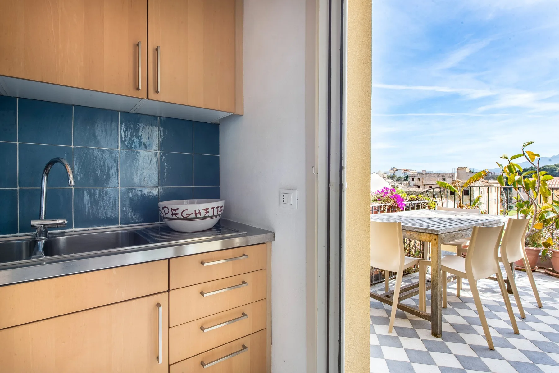 A compact kitchen opens onto a sunny terrace with a dining table and chairs.