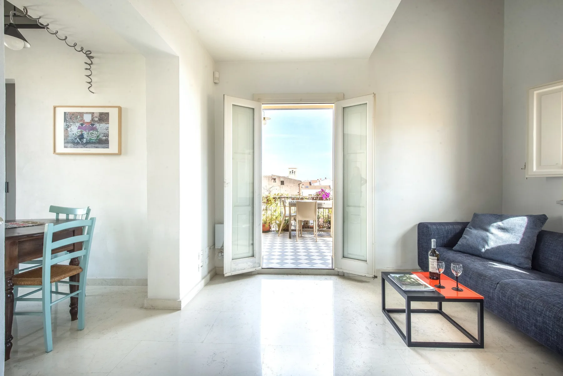 A bright living area opens onto a balcony, with seating and a small dining table.