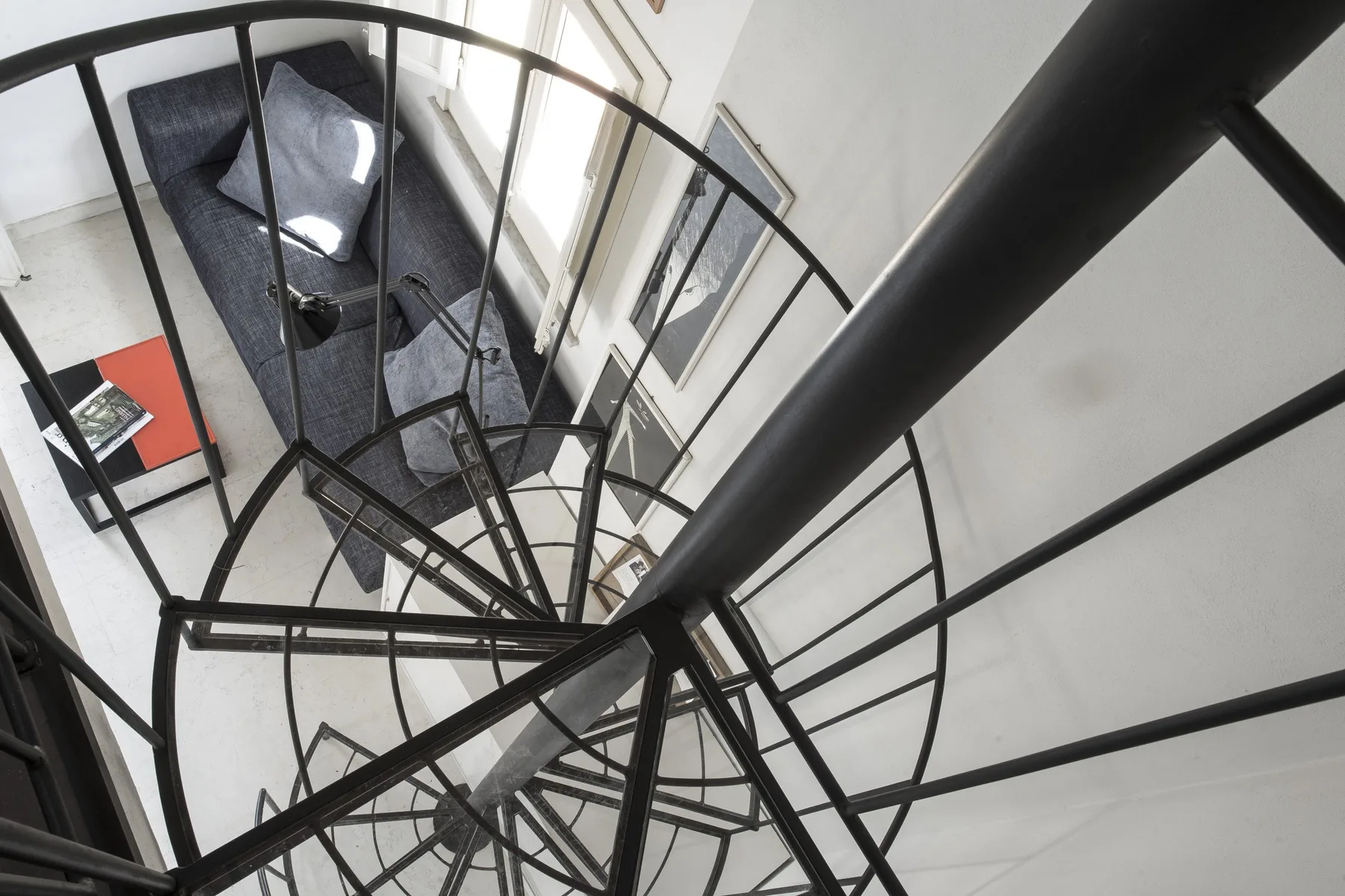 A spiral staircase overlooks a sitting area with dark seating.