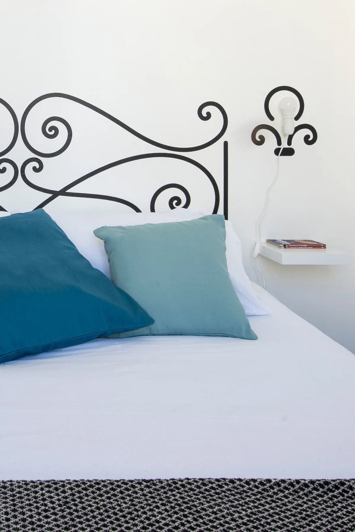 A bedroom with white bedding and teal pillows beneath a decorative black headboard.