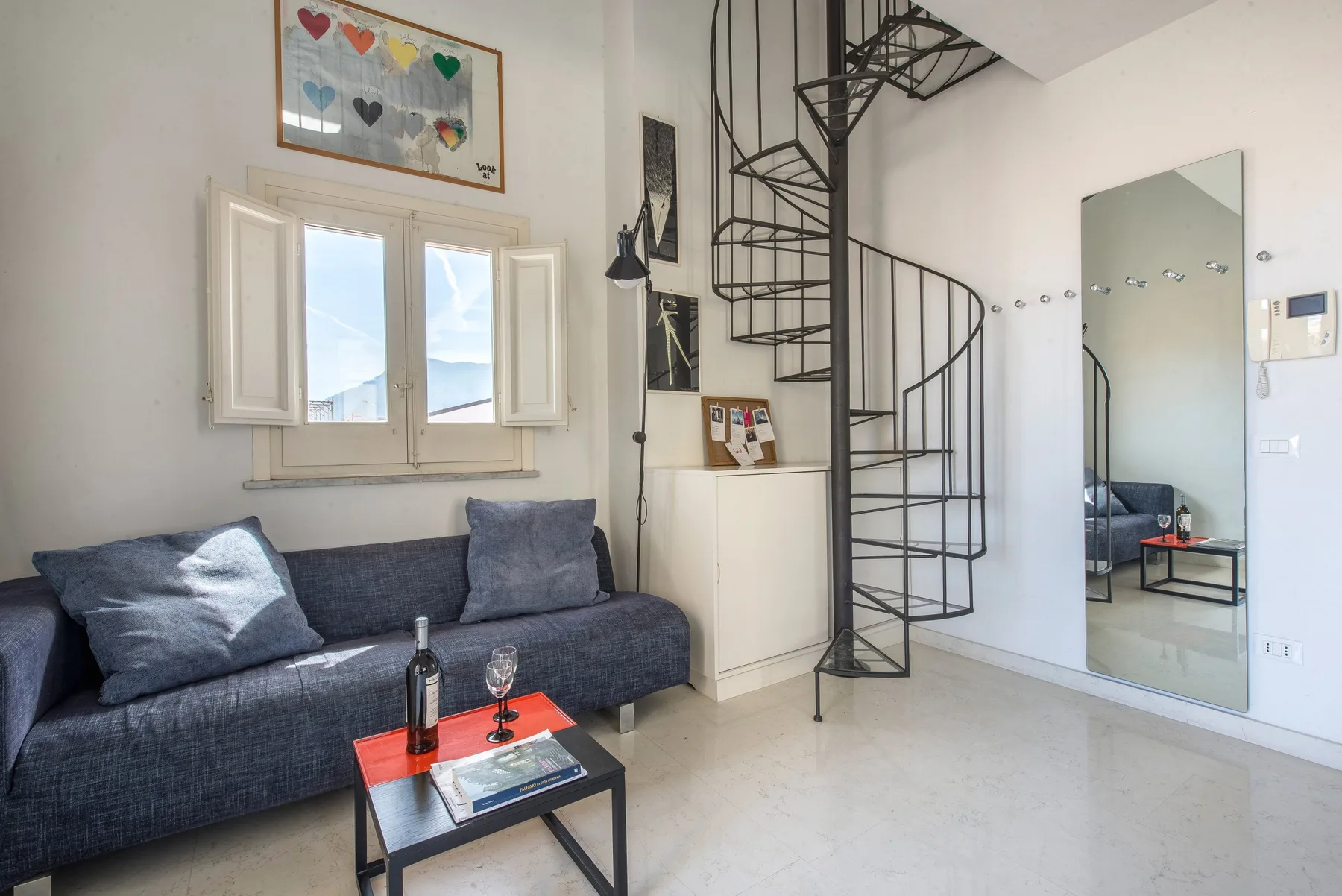 A living room with a dark sofa, a low table, and a spiral staircase.