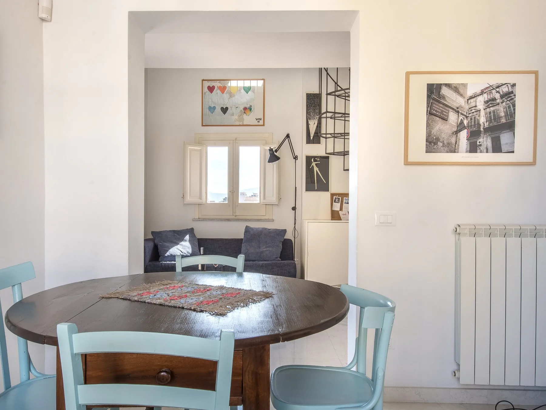 A dining area with a round table and pale blue chairs, beside a small sitting area.