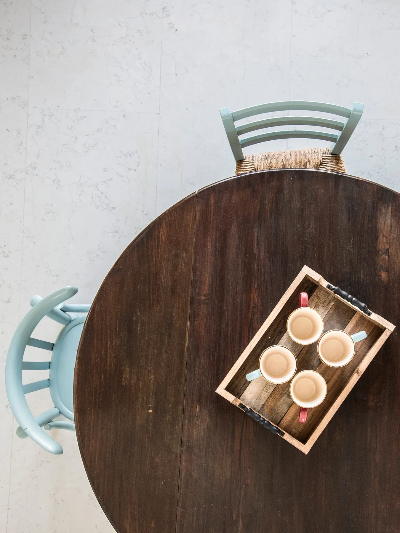 A round dining table with a wooden serving tray and pale blue seating.