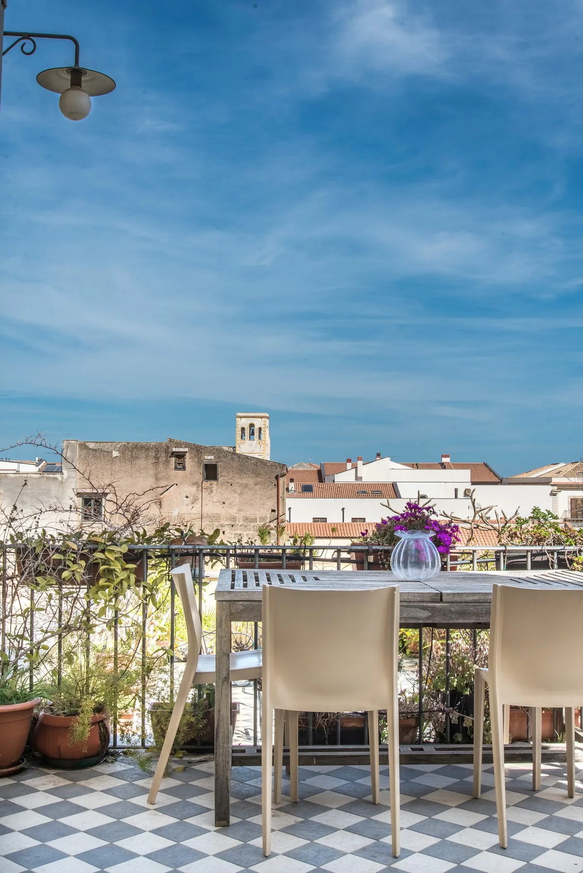 A rooftop terrace with outdoor seating, potted plants, and a broad view of the sky.