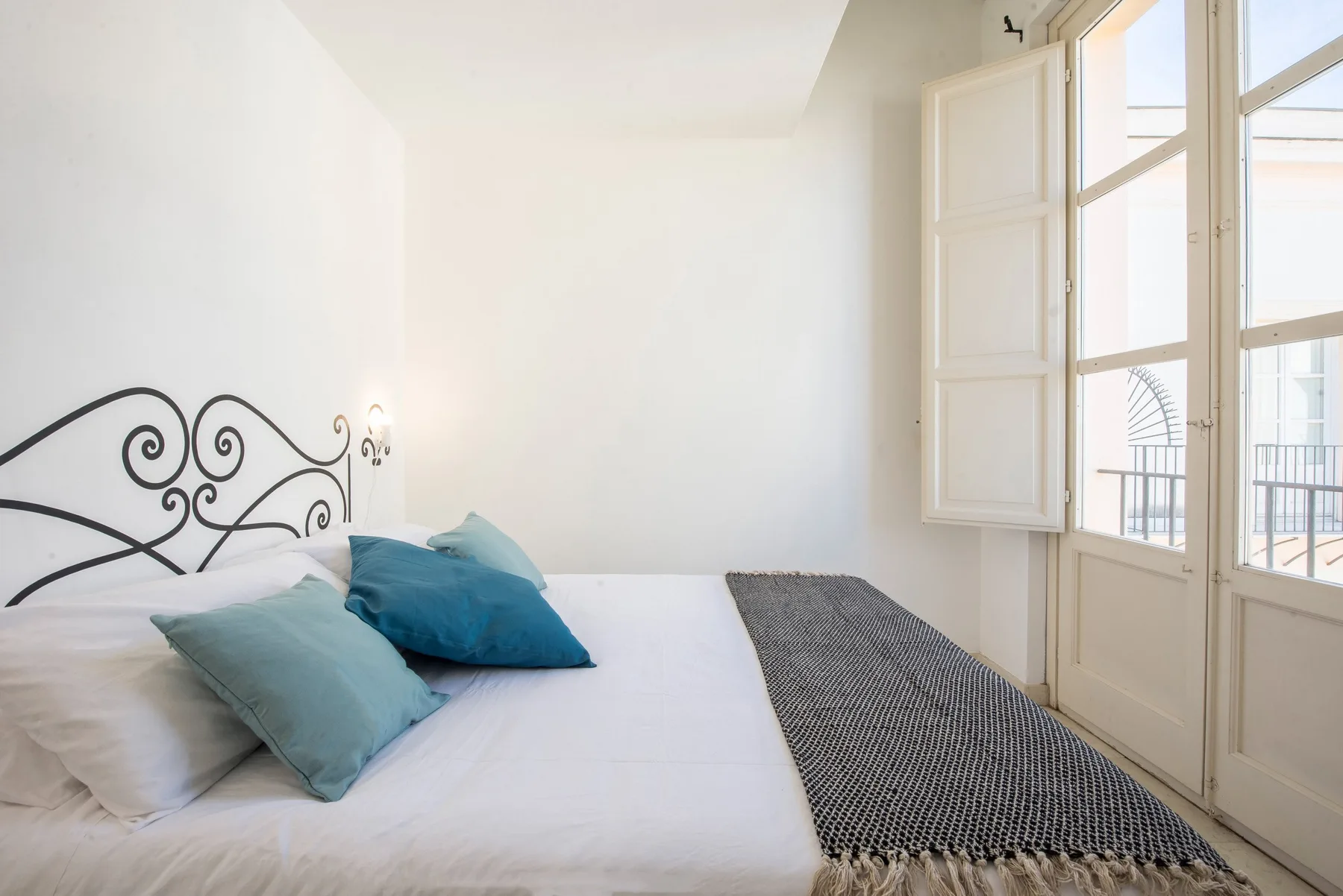 A bright bedroom with a bed, blue pillows, and tall windows.