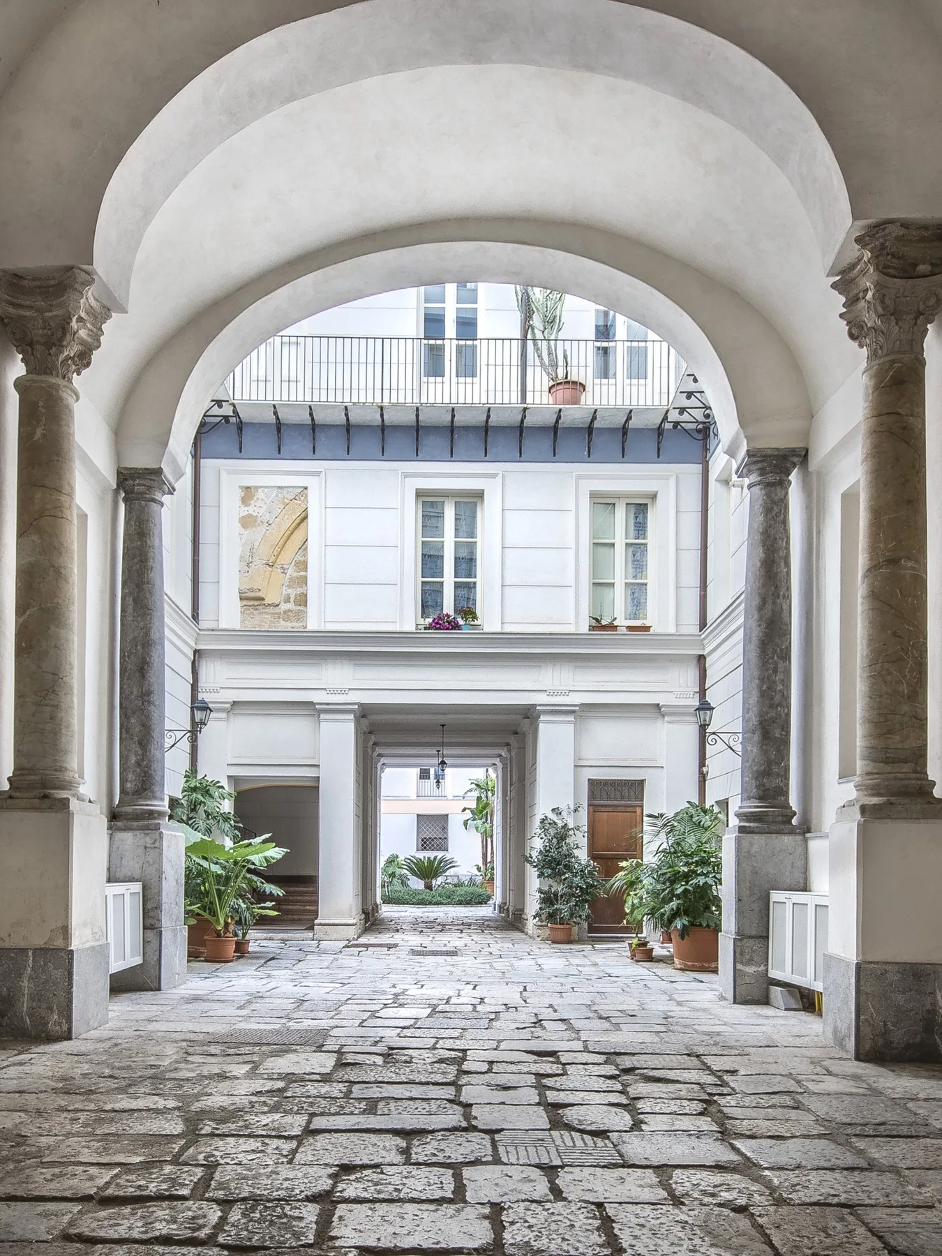 A stone passage with arched columns opens onto a courtyard with potted plants.