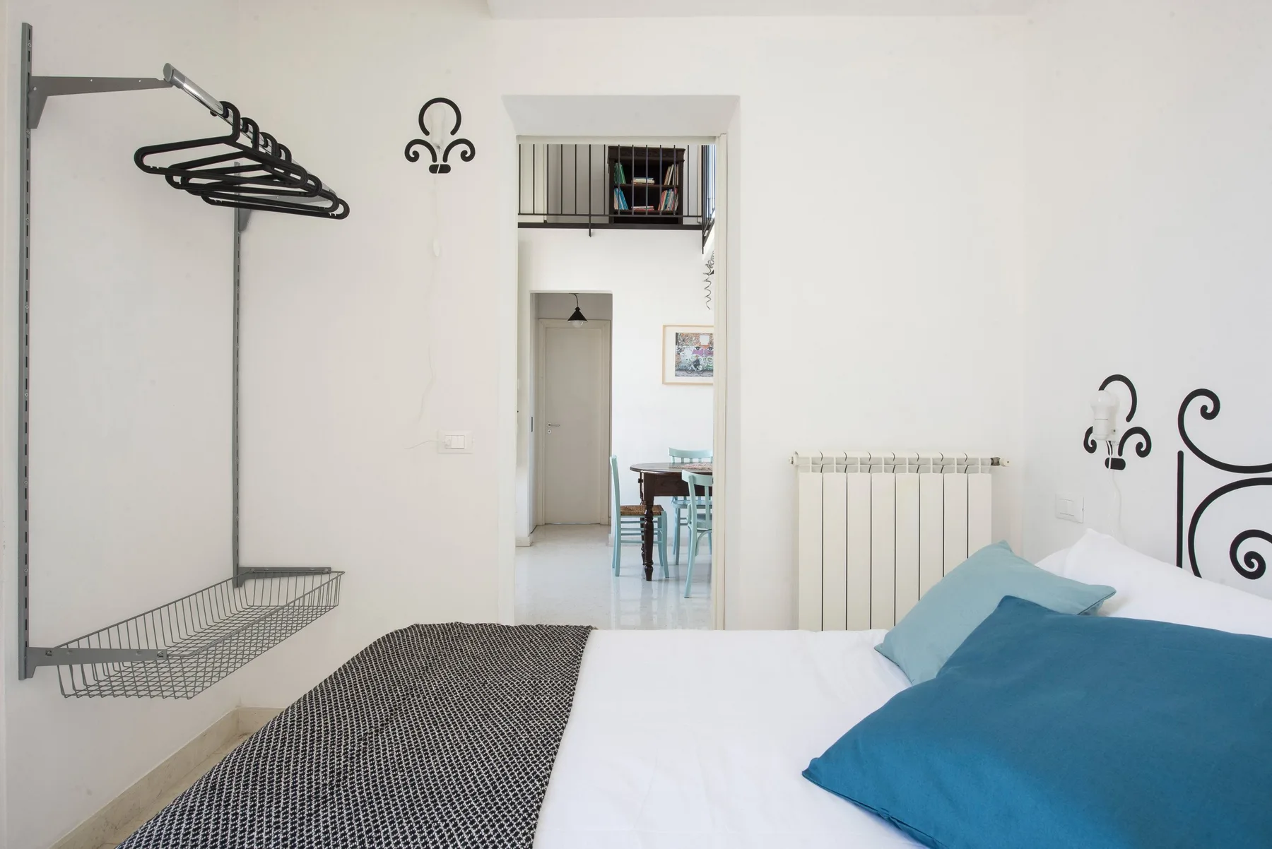A bright bedroom with a bed, blue pillows, and a wall-mounted clothes rack.