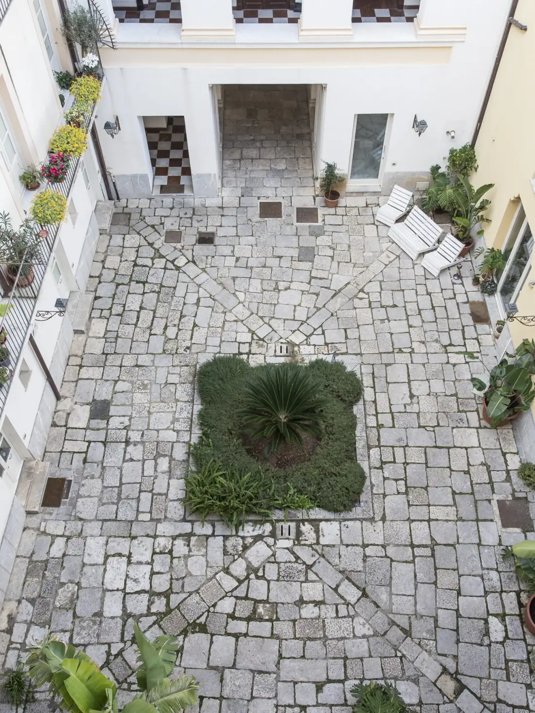 A paved courtyard with a central planted bed and white seating along the side.