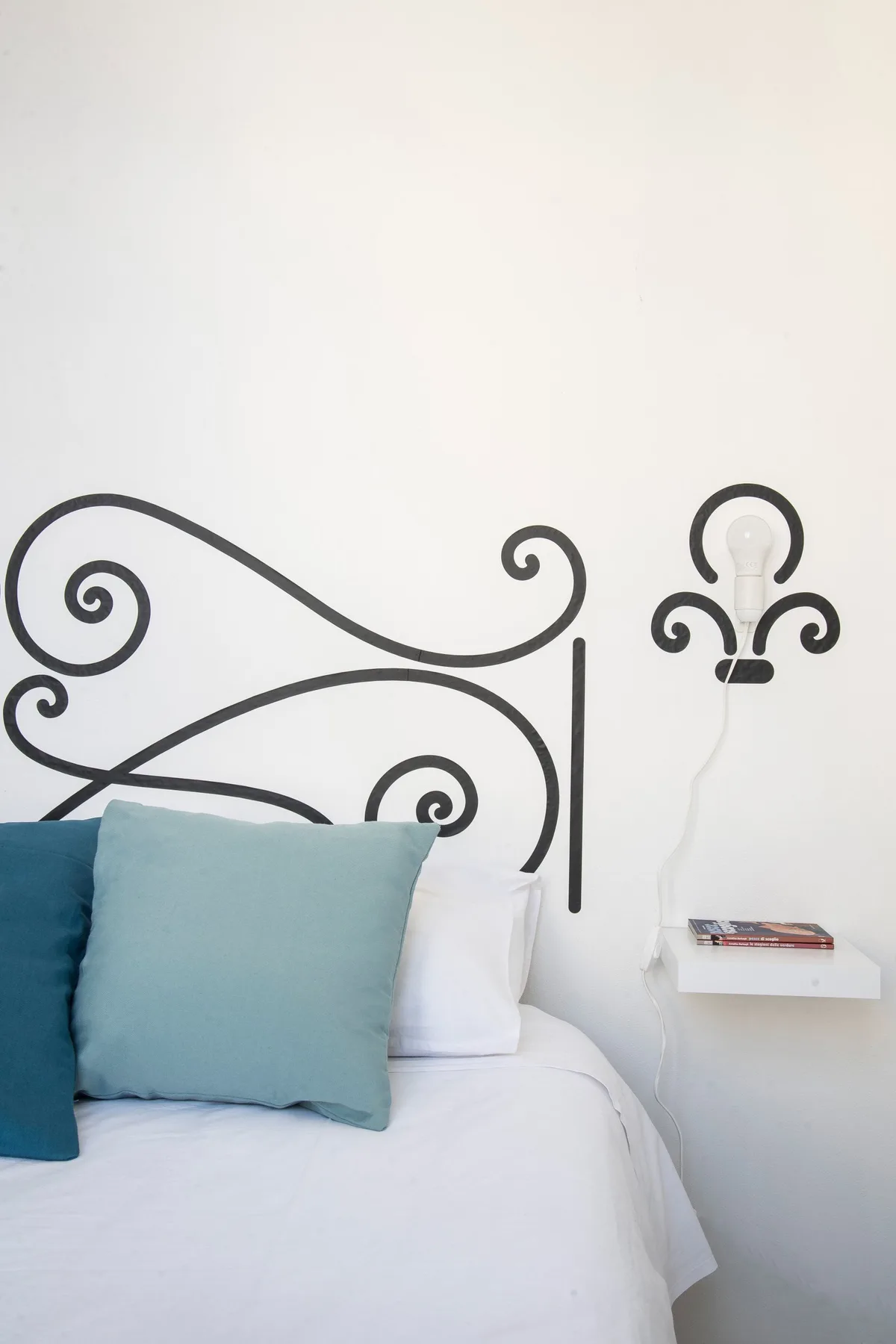 A bed with blue pillows sits against a wall decorated with dark curling lines.