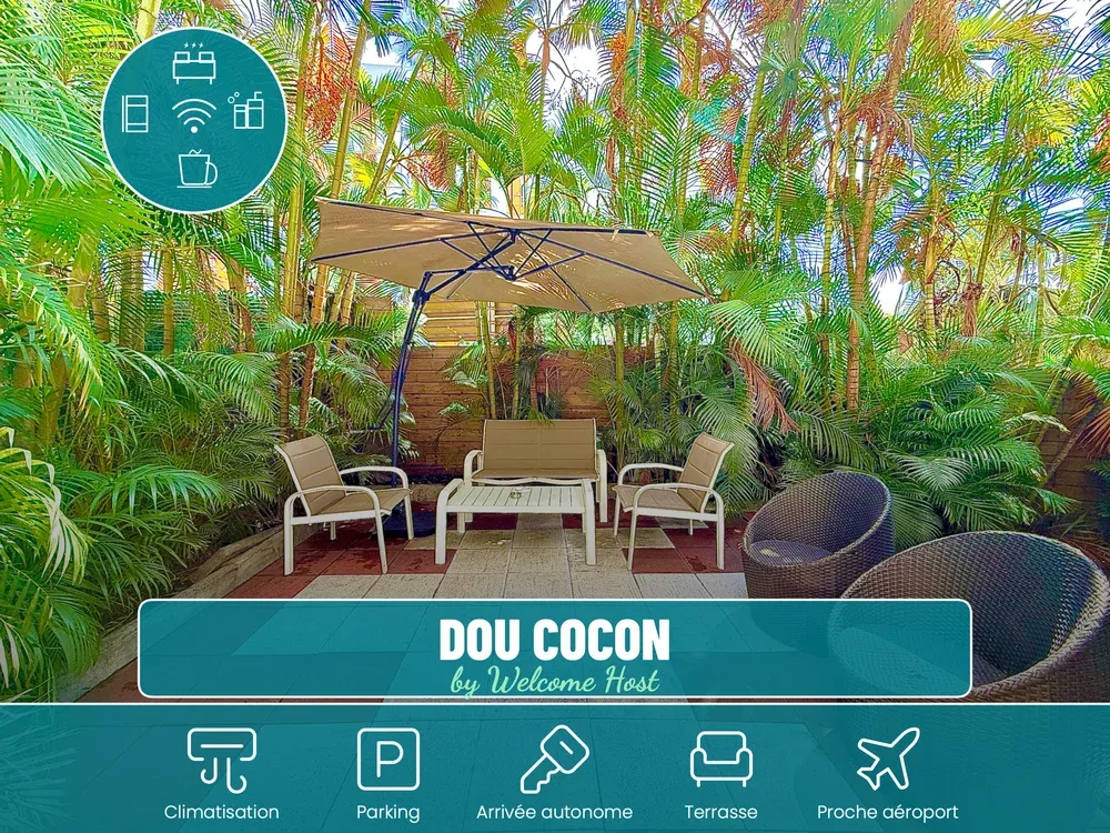 Outdoor patio seating sits beneath a large umbrella amid dense tropical greenery.