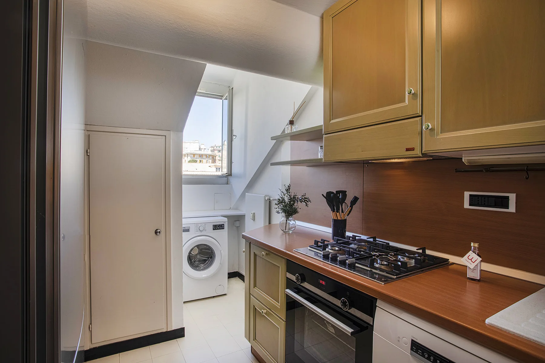 Una cocina compacta con armarios de madera, una placa de cocina y una lavadora.