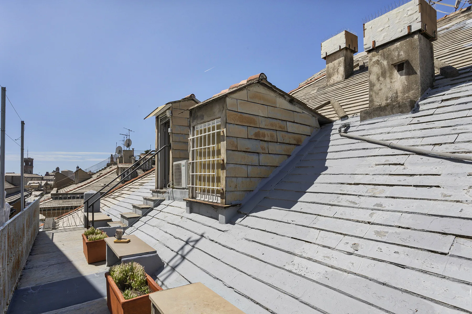 Una terraza en la azotea con techos inclinados y jardineras bajo un cielo despejado.