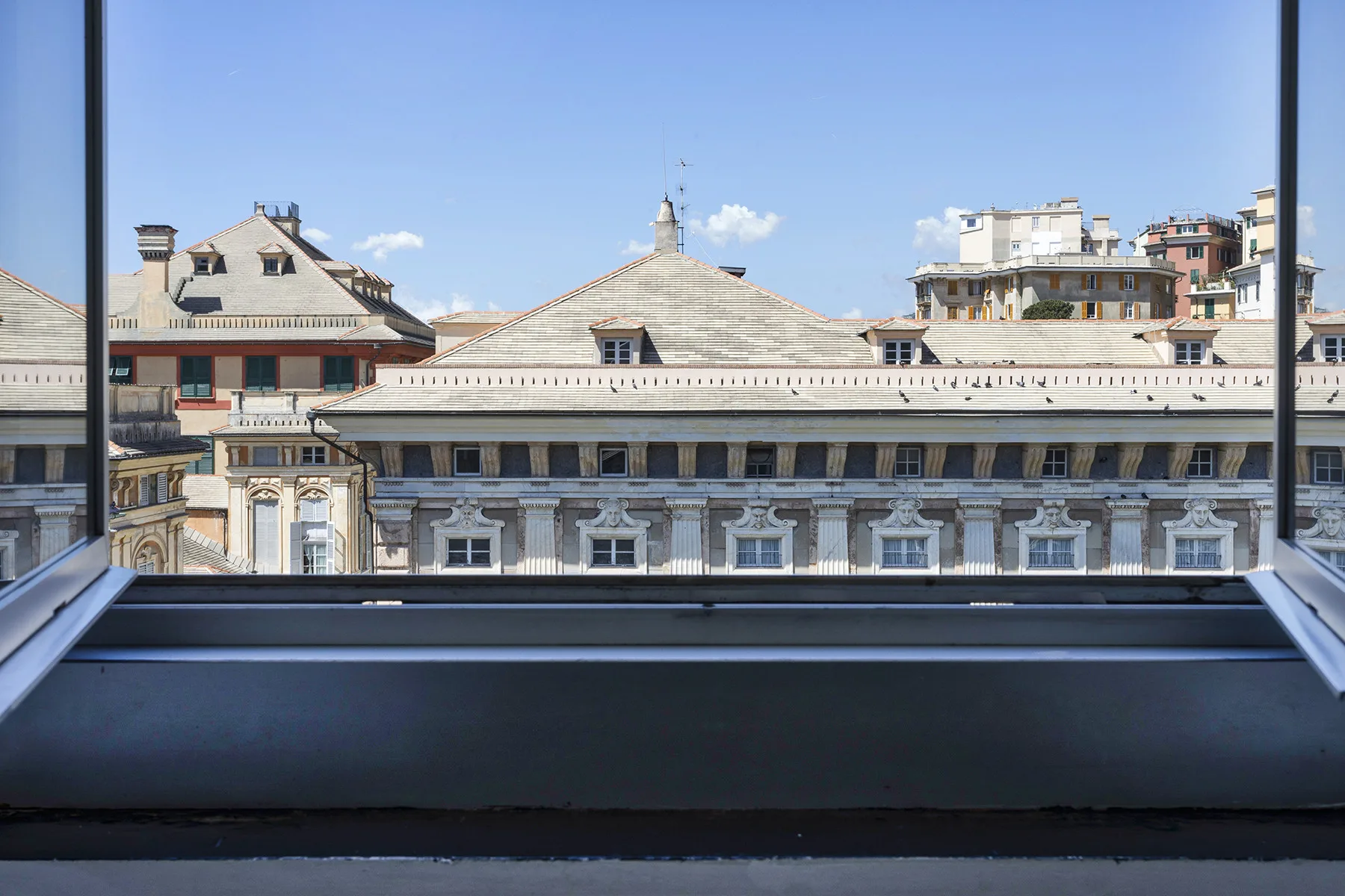 Vista de la ciudad desde una ventana, con tejados históricos bajo un cielo despejado.