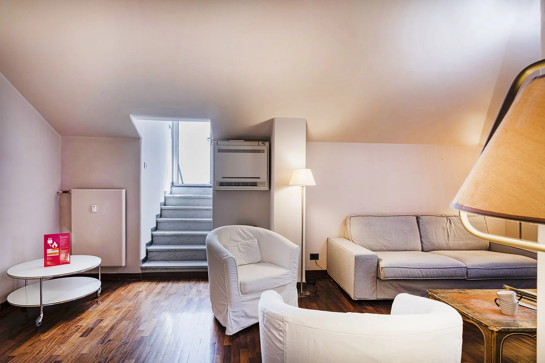 Una sala de estar con asientos, una lámpara de pie y una escalera.