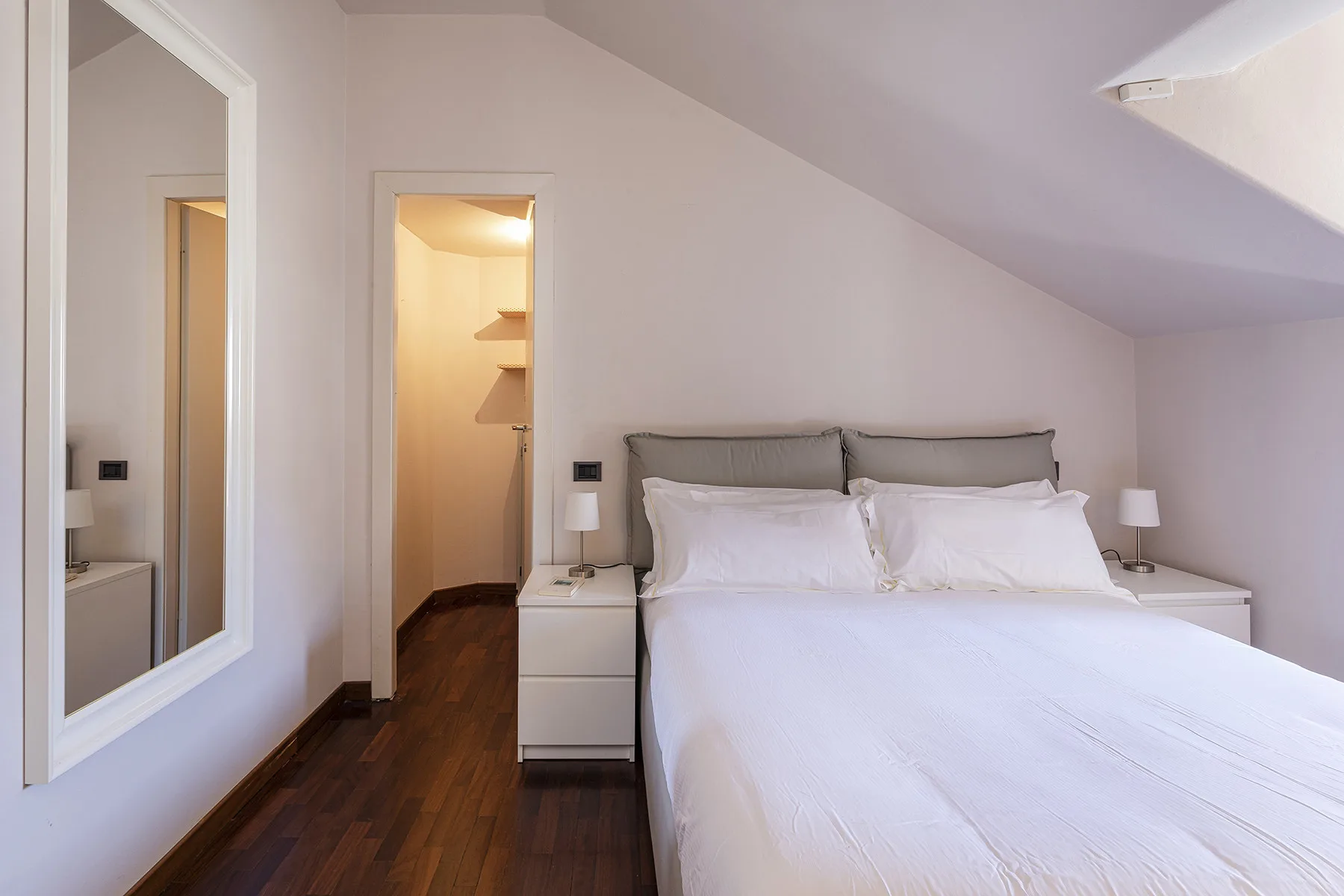 Un dormitorio con una cama tendida y mesitas de noche bajo un techo inclinado.