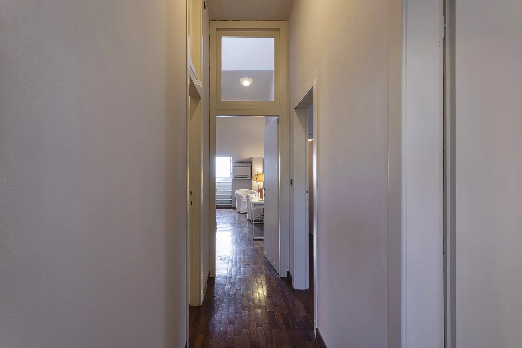 Un pasillo estrecho con suelo de madera oscura conduce a una habitación amueblada.