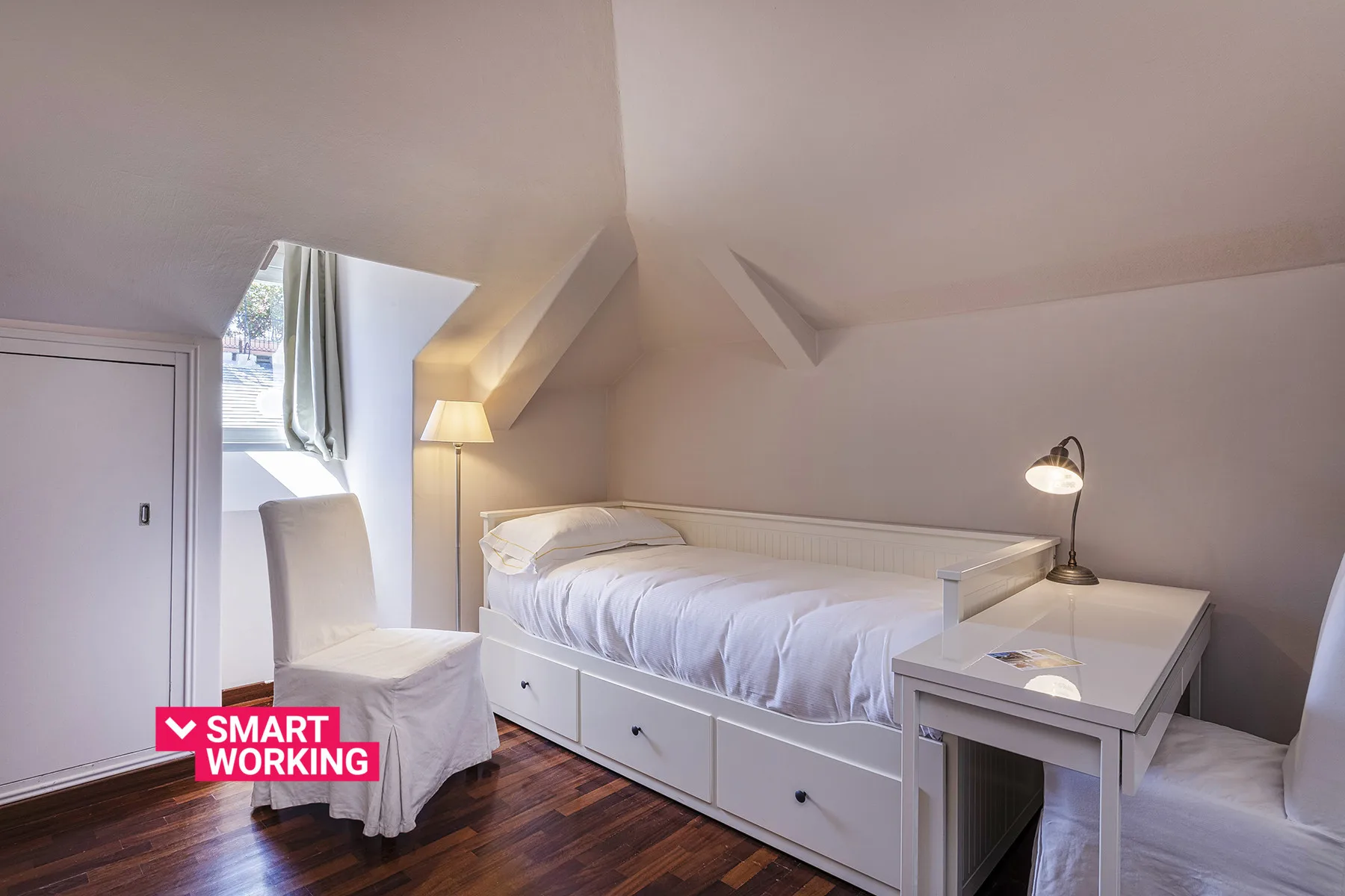 Un dormitorio abuhardillado luminoso con cama, asiento y un pequeño escritorio.