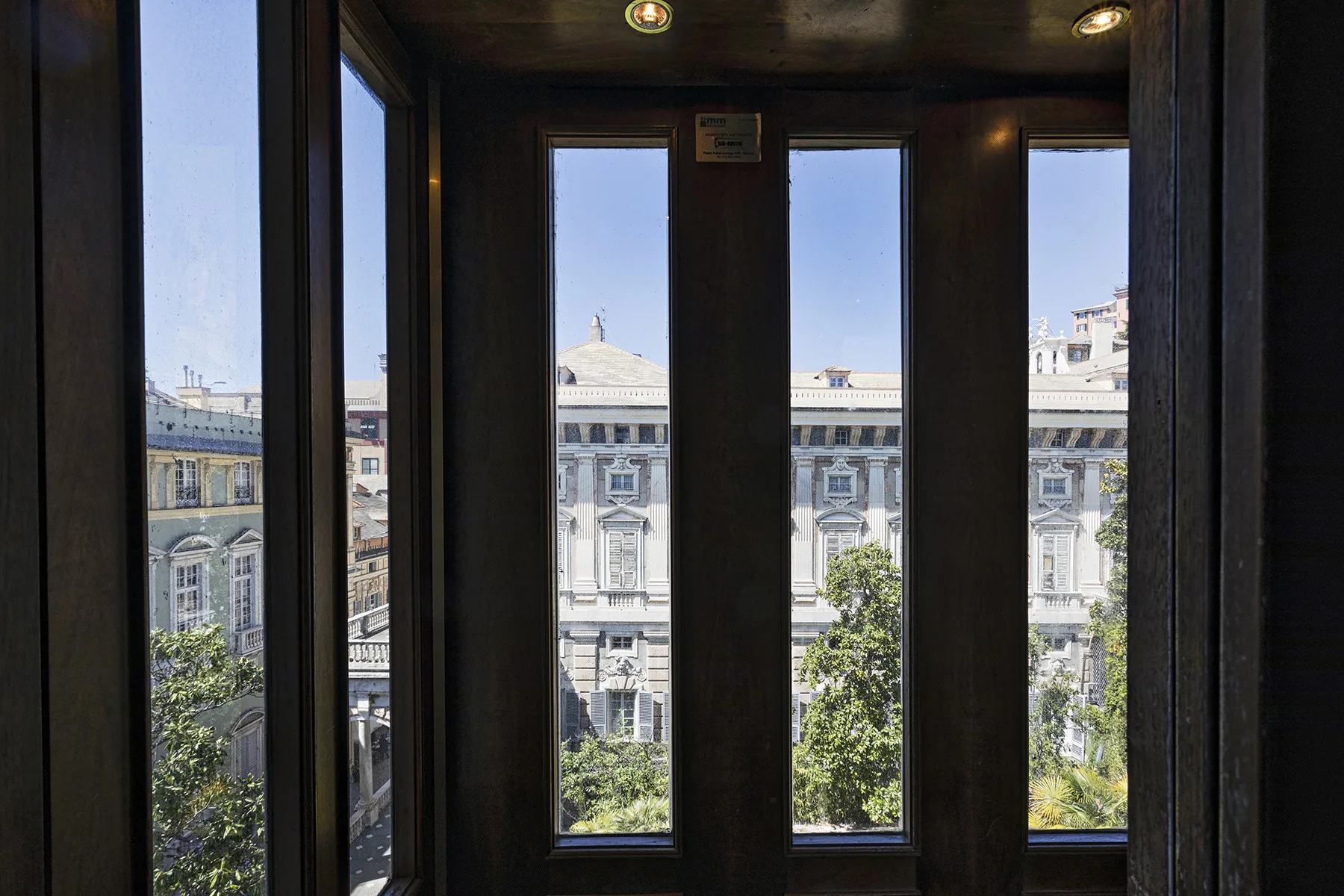 Ventanas altas dan a edificios vecinos y árboles frondosos.