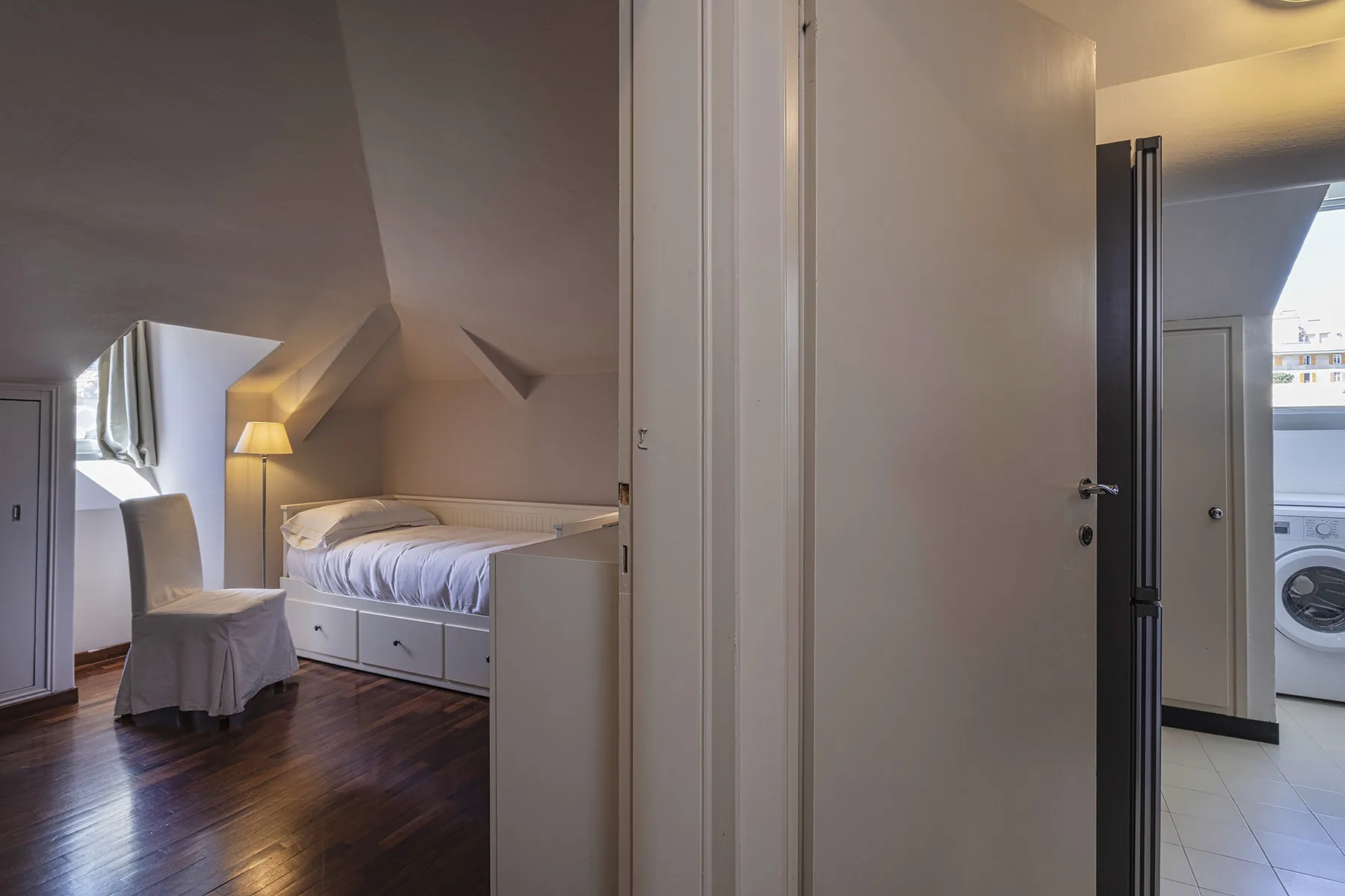 Un dormitorio con una cama y una silla bajo un techo inclinado.