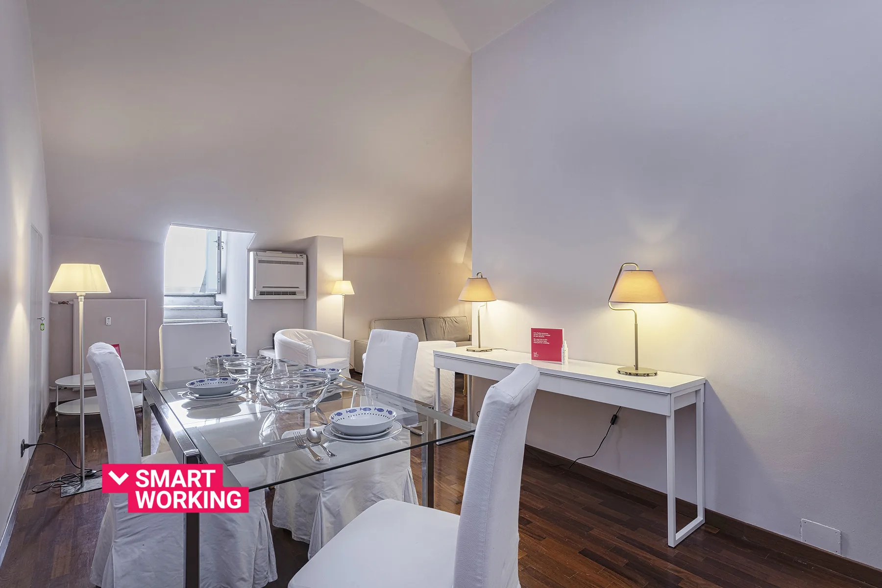 Una luminosa zona de comedor y trabajo con una mesa de cristal y un escritorio largo.