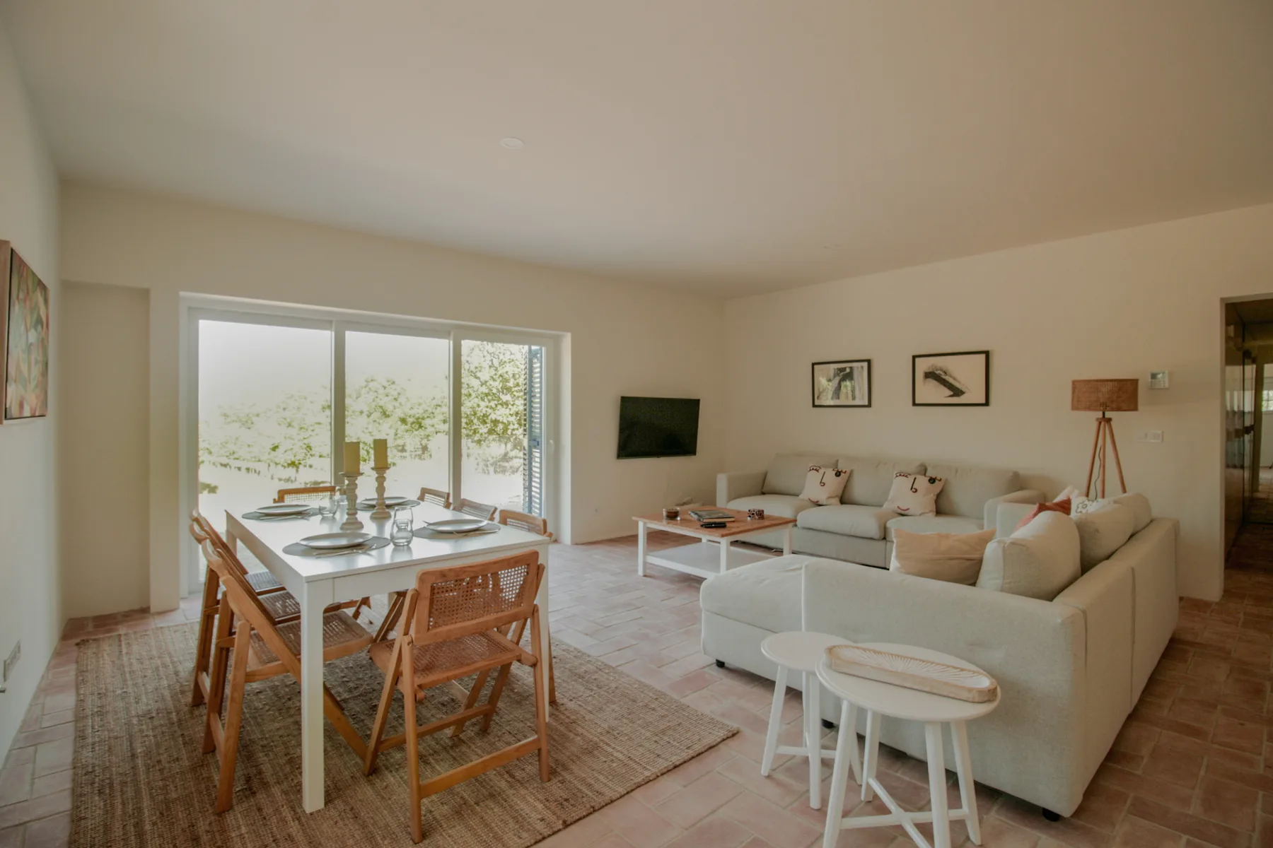 A bright living and dining area with a table, seating, and large windows.