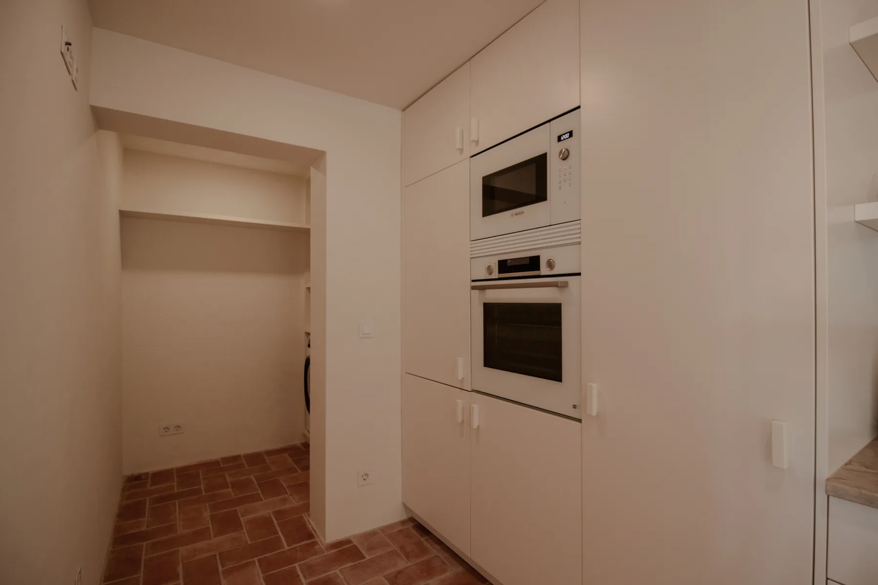 A kitchen with built-in appliances and white cabinets beside an open shelving alcove.