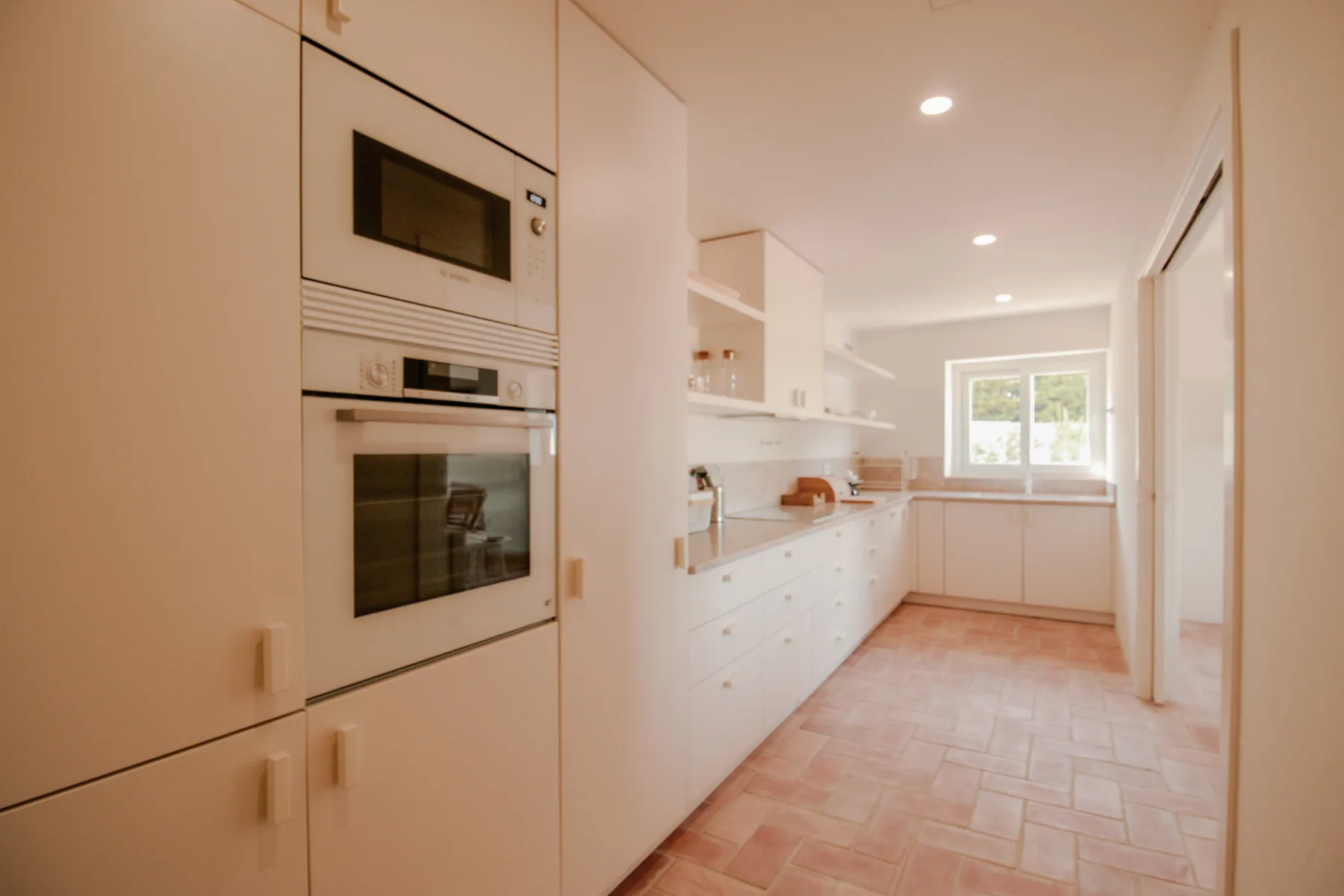 A bright kitchen with white cabinetry, built-in appliances, and a window at the far end.