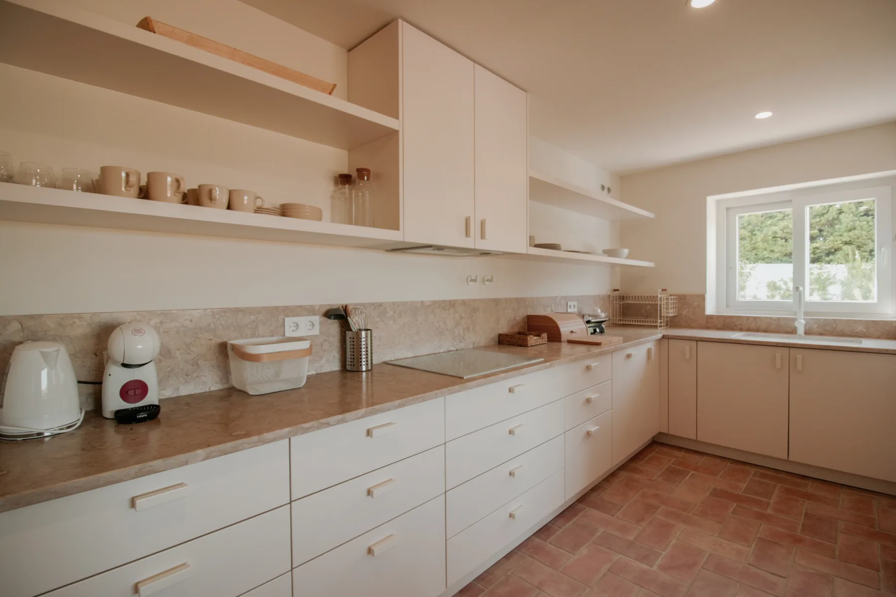A bright kitchen with white cabinetry, a long countertop, and a window.