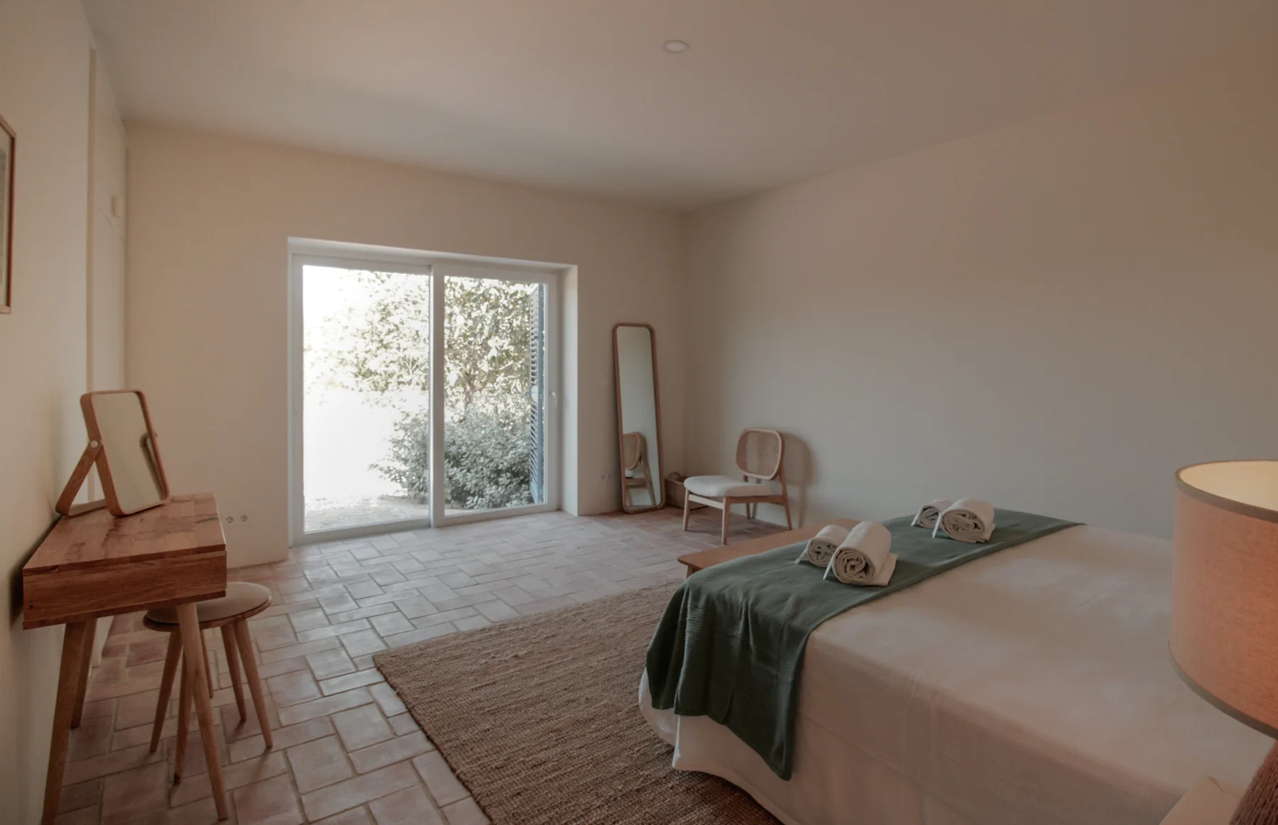 A bedroom with a bed, a writing desk, and a sliding glass door.
