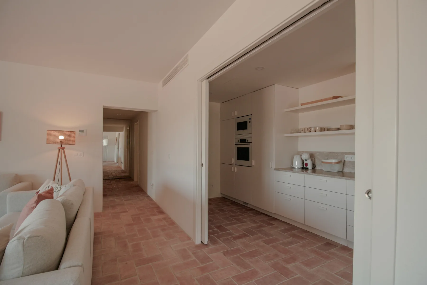 A bright open-plan room with a kitchen, seating area, and tiled floor.