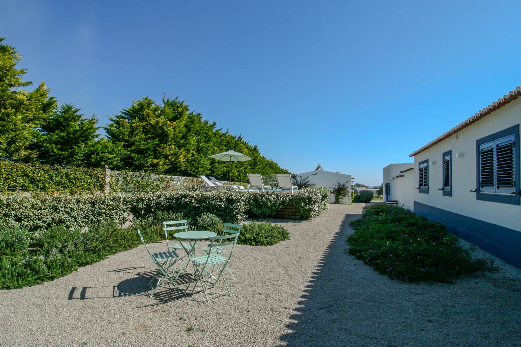 A gravel courtyard with outdoor seating beside a white house and garden.
