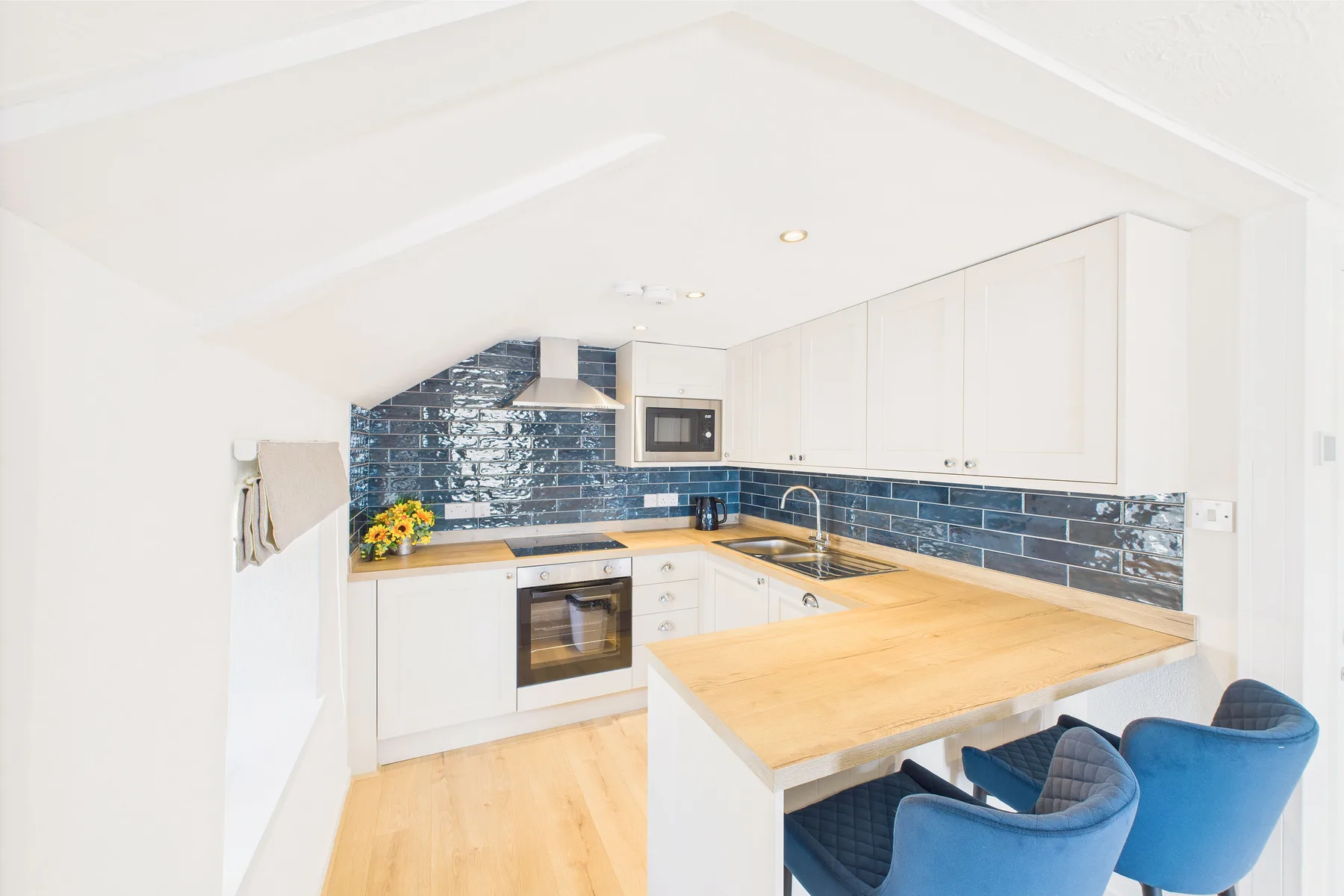 Una cocina luminosa con gabinetes blancos, azulejos azules y una isla con cubierta de madera.