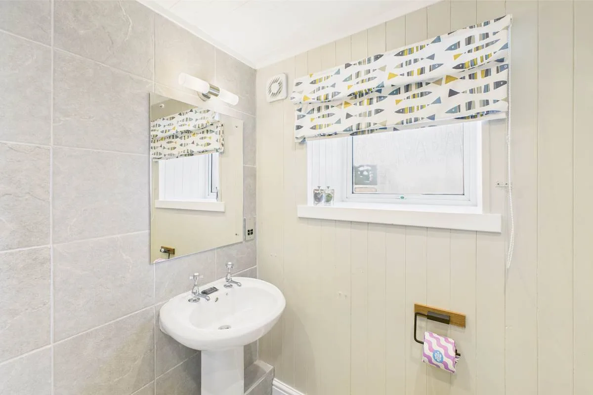 Baño con lavabo de pedestal y ventana con una cenefa estampada.