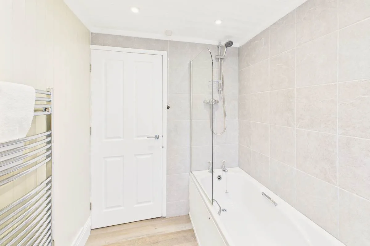 Un baño alicatado con bañera y ducha montada en la pared.